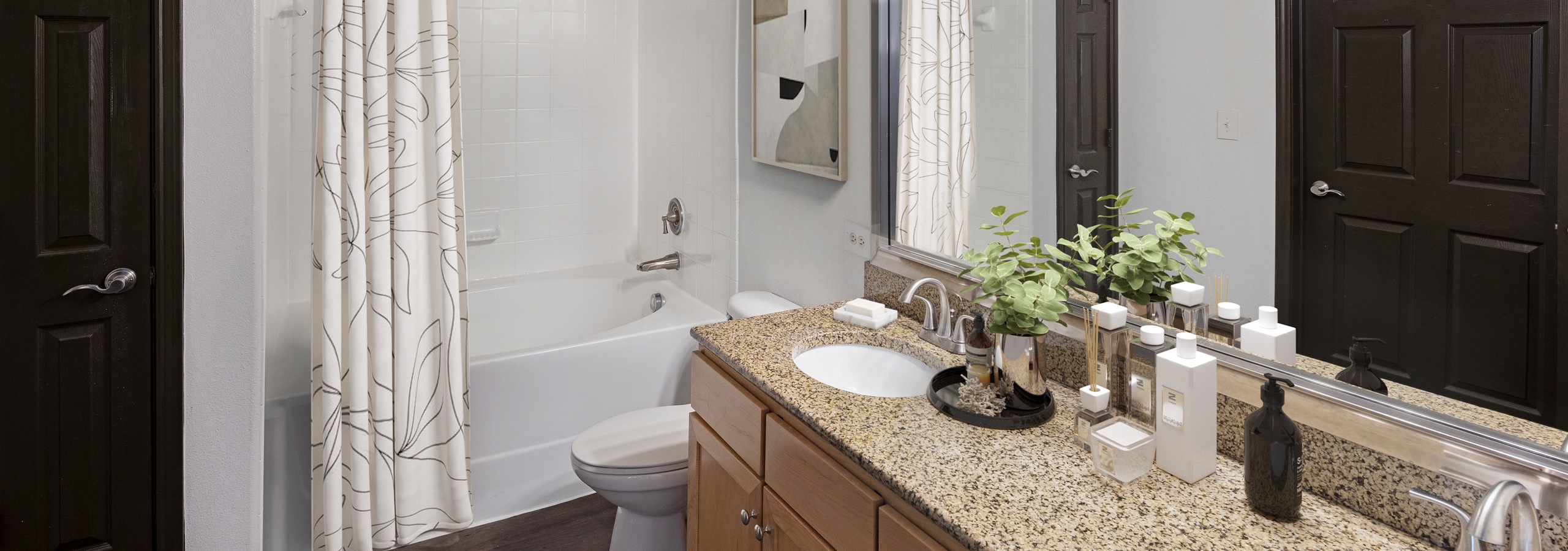 AMLI 300 apartment bathroom with granite double vanity with large mirror above and white soaking tub with curtain