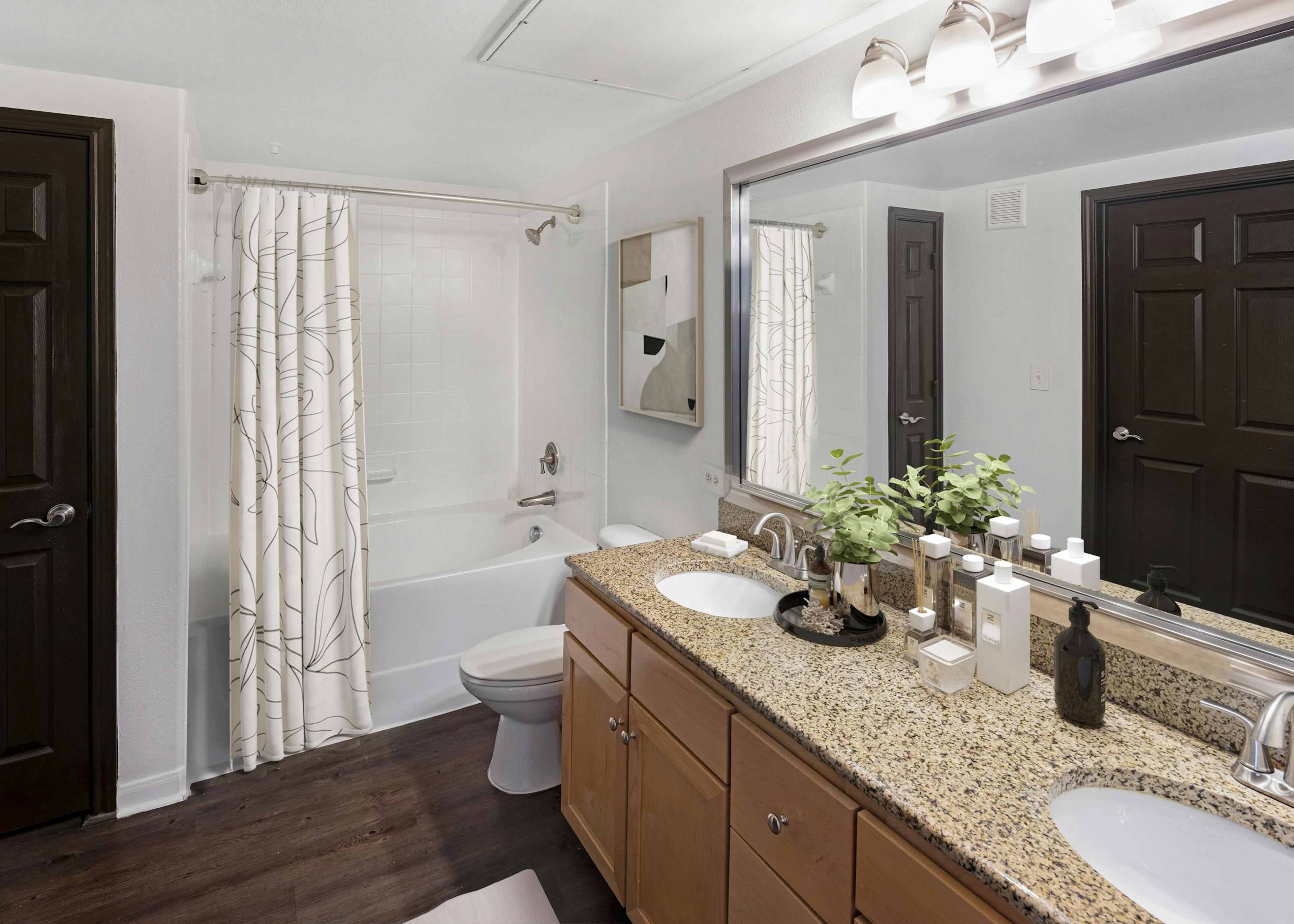 AMLI 300 apartment bathroom with granite double vanity with large mirror above and white soaking tub with curtain