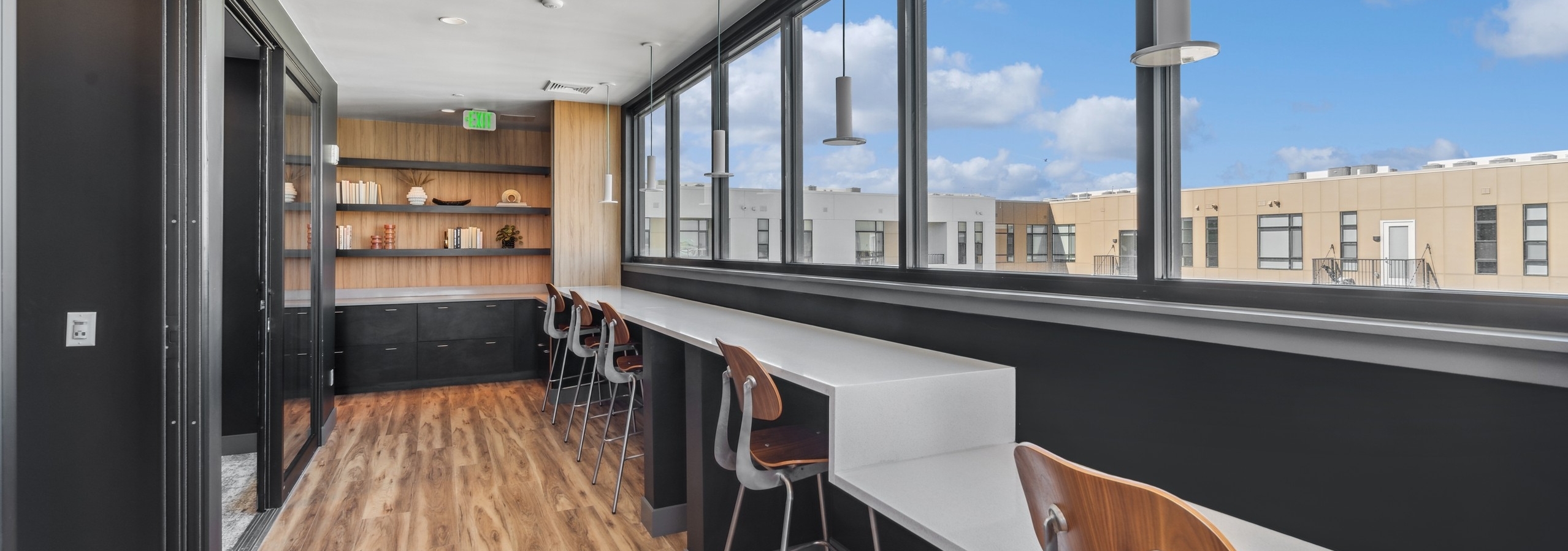 AMLI Broadway Park library lounge with wood floors and white countertop bar seating overlooking wall of windows to courtyard