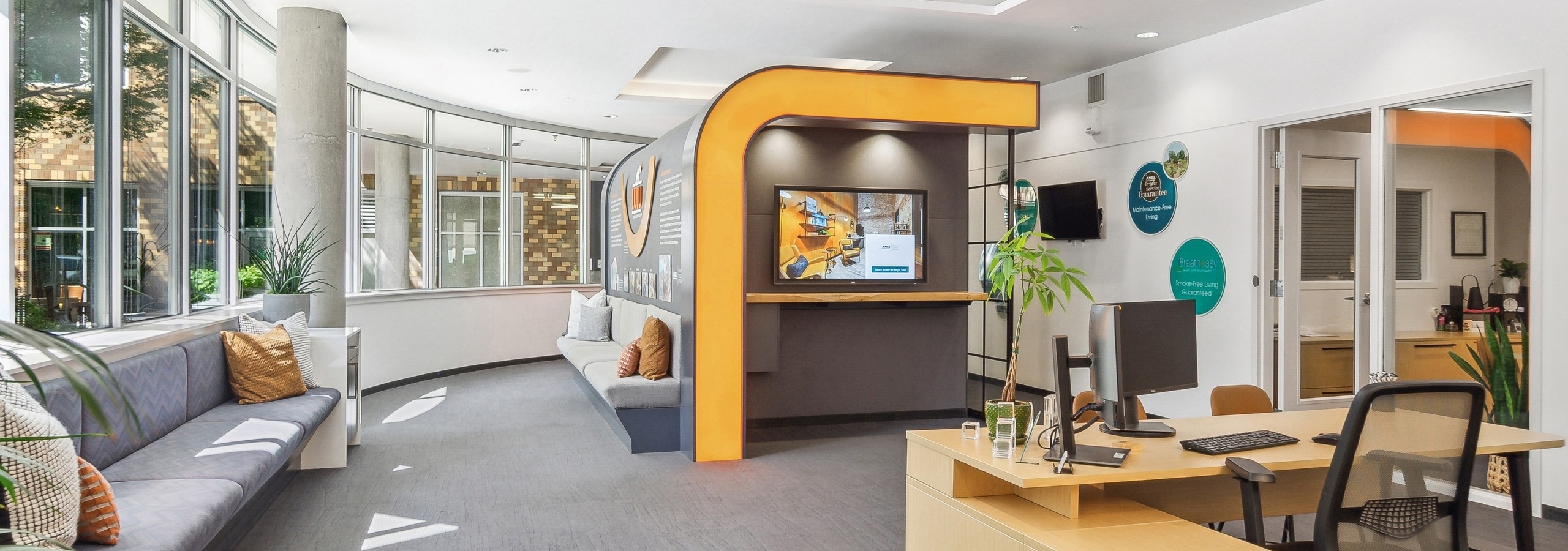 The leasing office at AMLI South Lake Union with high ceilings and seating and a desk with bright artwork and mounted TV