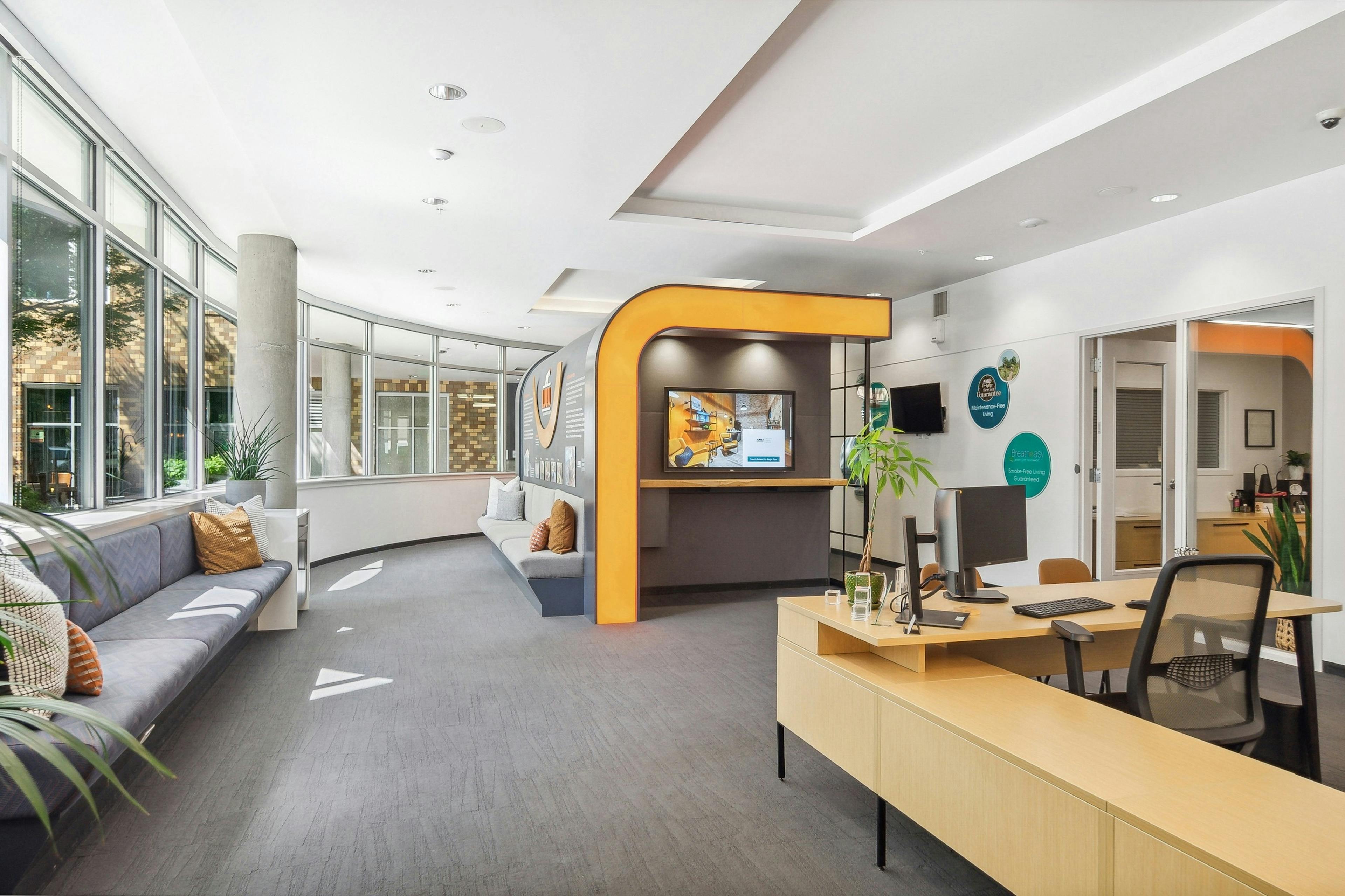 The leasing office at AMLI South Lake Union with high ceilings and seating and a desk with bright artwork and mounted TV