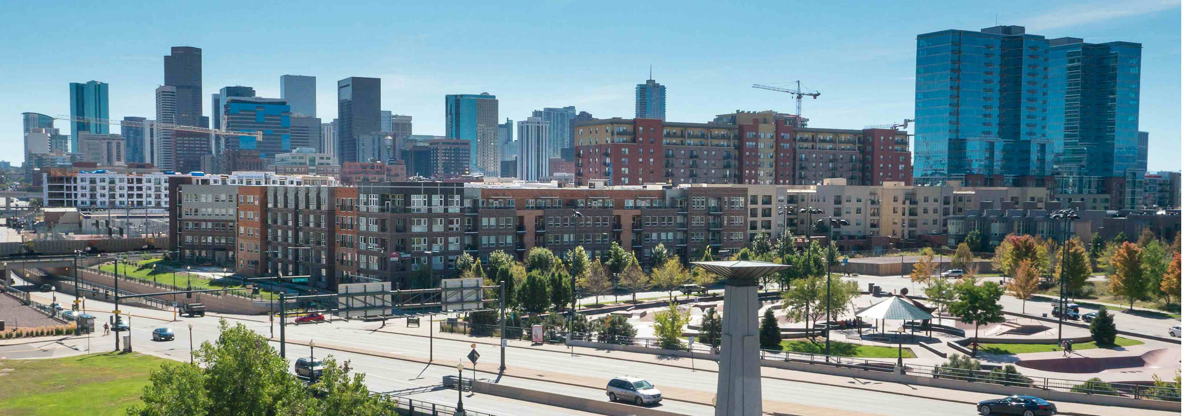 Ariel view of AMLI Riverfront Park apartments with the downtown Denver skyline and the Denver skate park and green trees