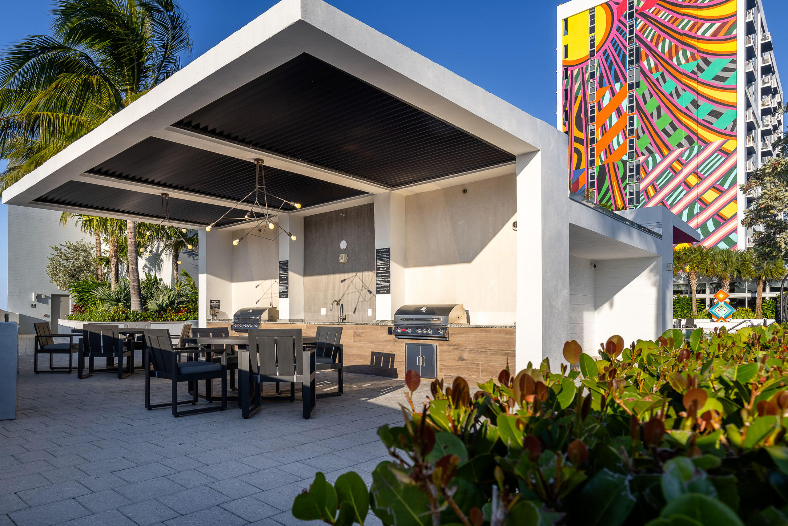 AMLI Midtown 29 grill station with 2 stainless grills and 2 brown tables with chairs and colorful building mural in rear