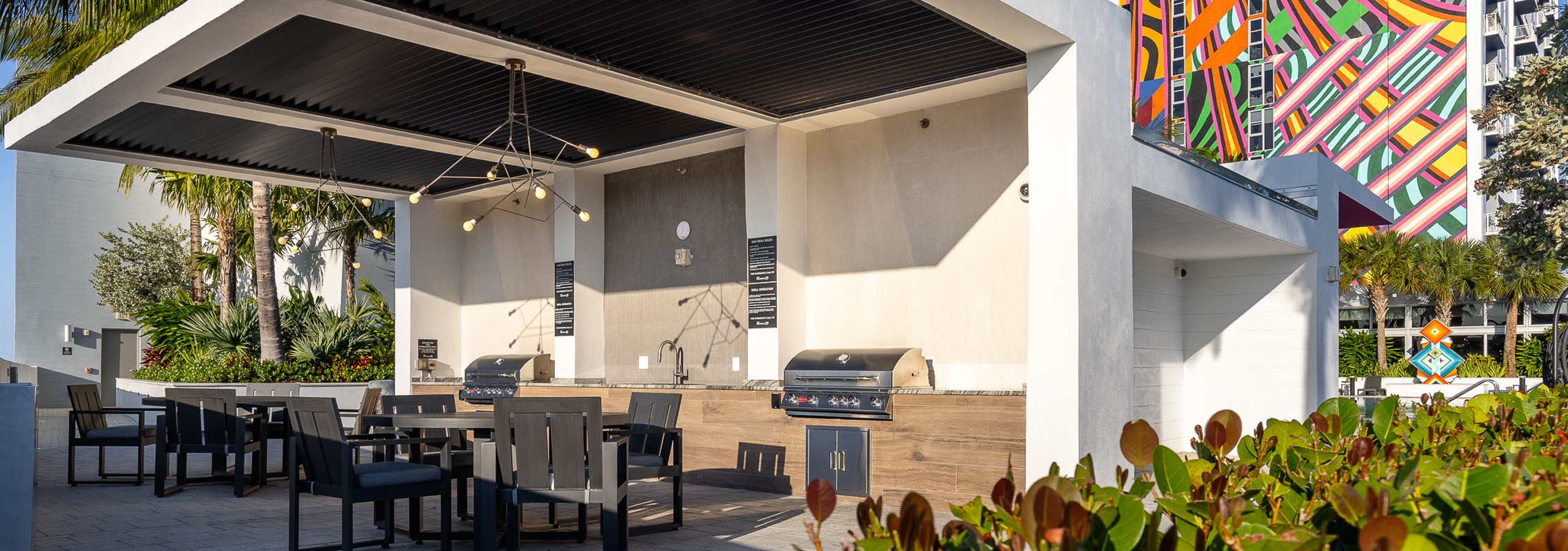 AMLI Midtown 29 grill station with 2 stainless grills and 2 brown tables with chairs and colorful building mural in rear