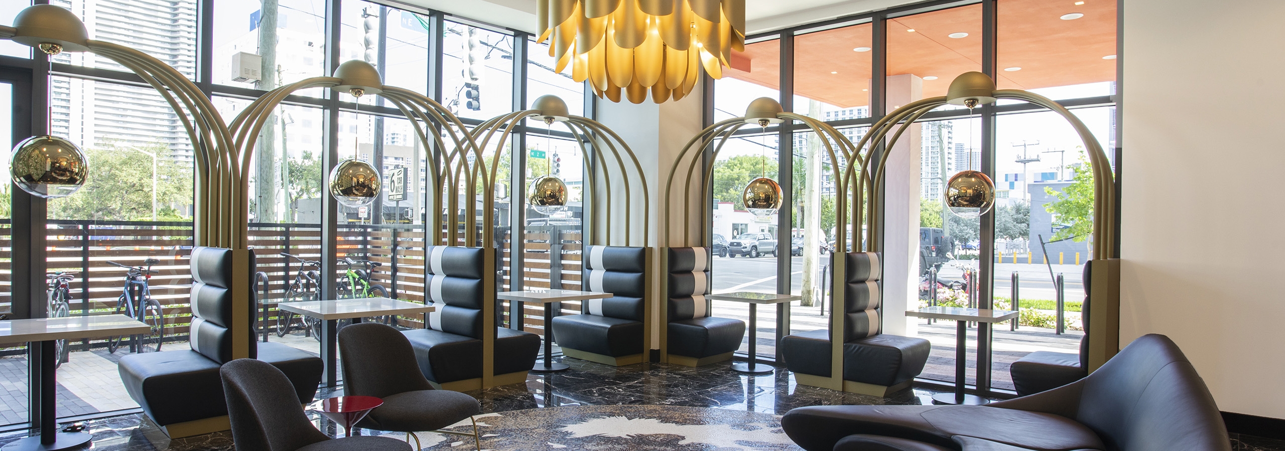 Lobby at AMLI Midtown Miami with black booths along 2 walls of windows with modern couch and large gold chandelier above