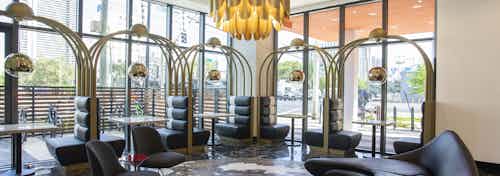 Lobby at AMLI Midtown Miami with black booths along 2 walls of windows with modern couch and large gold chandelier above
