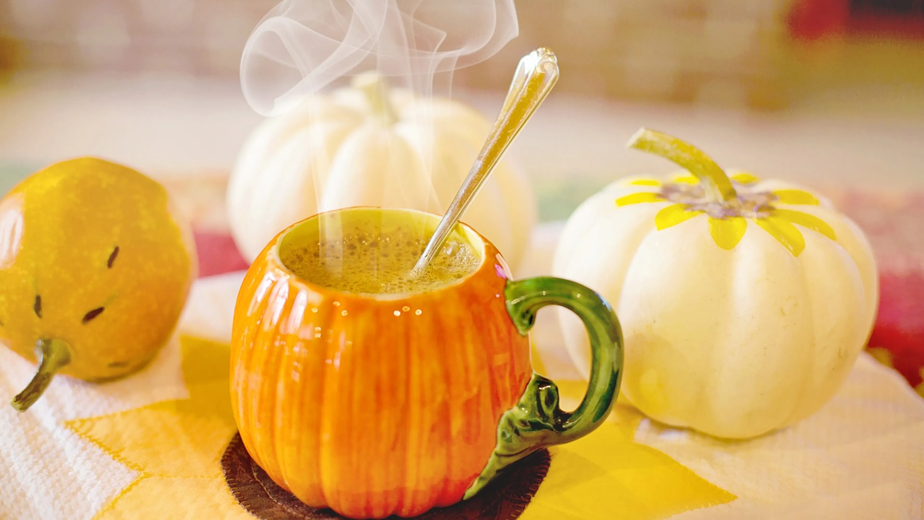 A large pumpkin shaped orange mug with a silver spoon inside and hot chocolate steaming inside