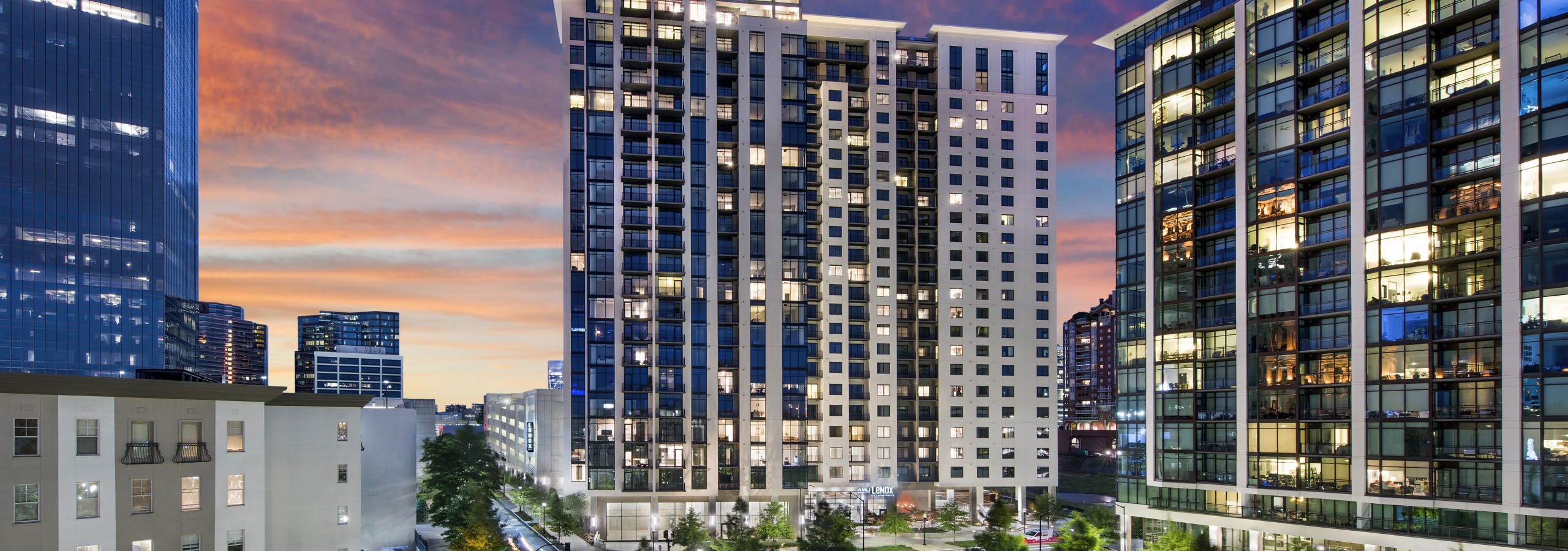 Nighttime exterior view of AMLI Lenox apartment building with brightly lit apartments overlooking Marie Simms Park
