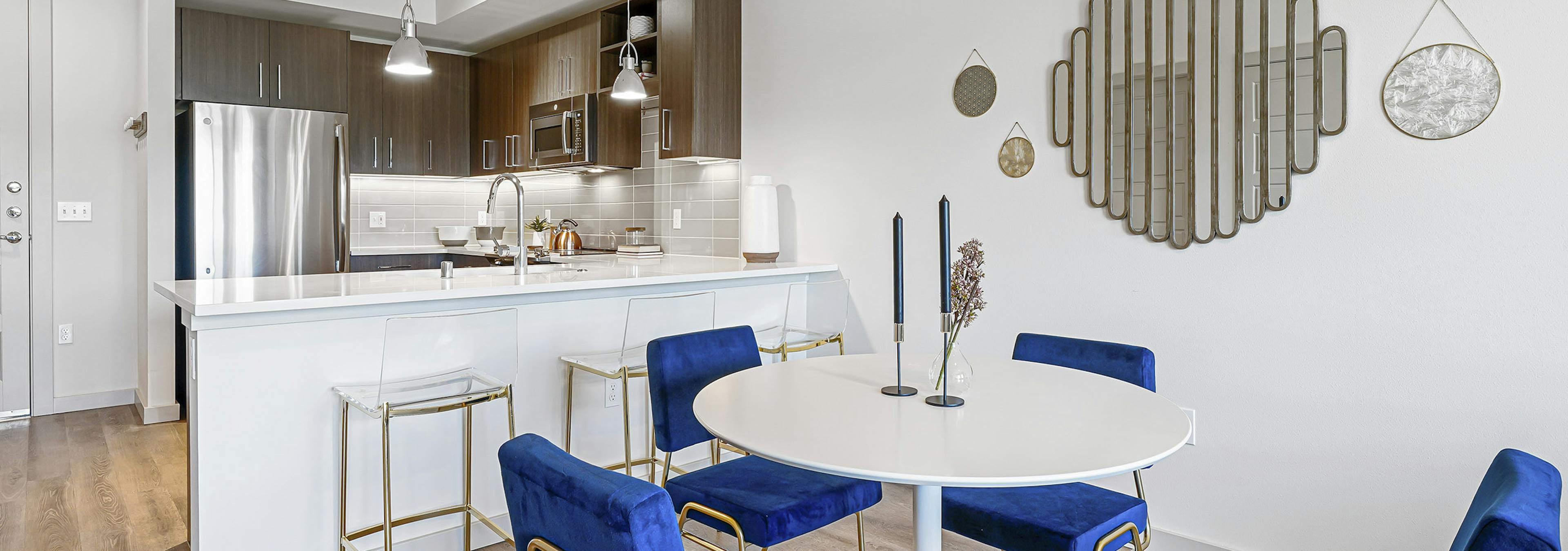 AMLI Spring District apartment kitchen with brown cabinets and dining room with white table and four blue chairs 