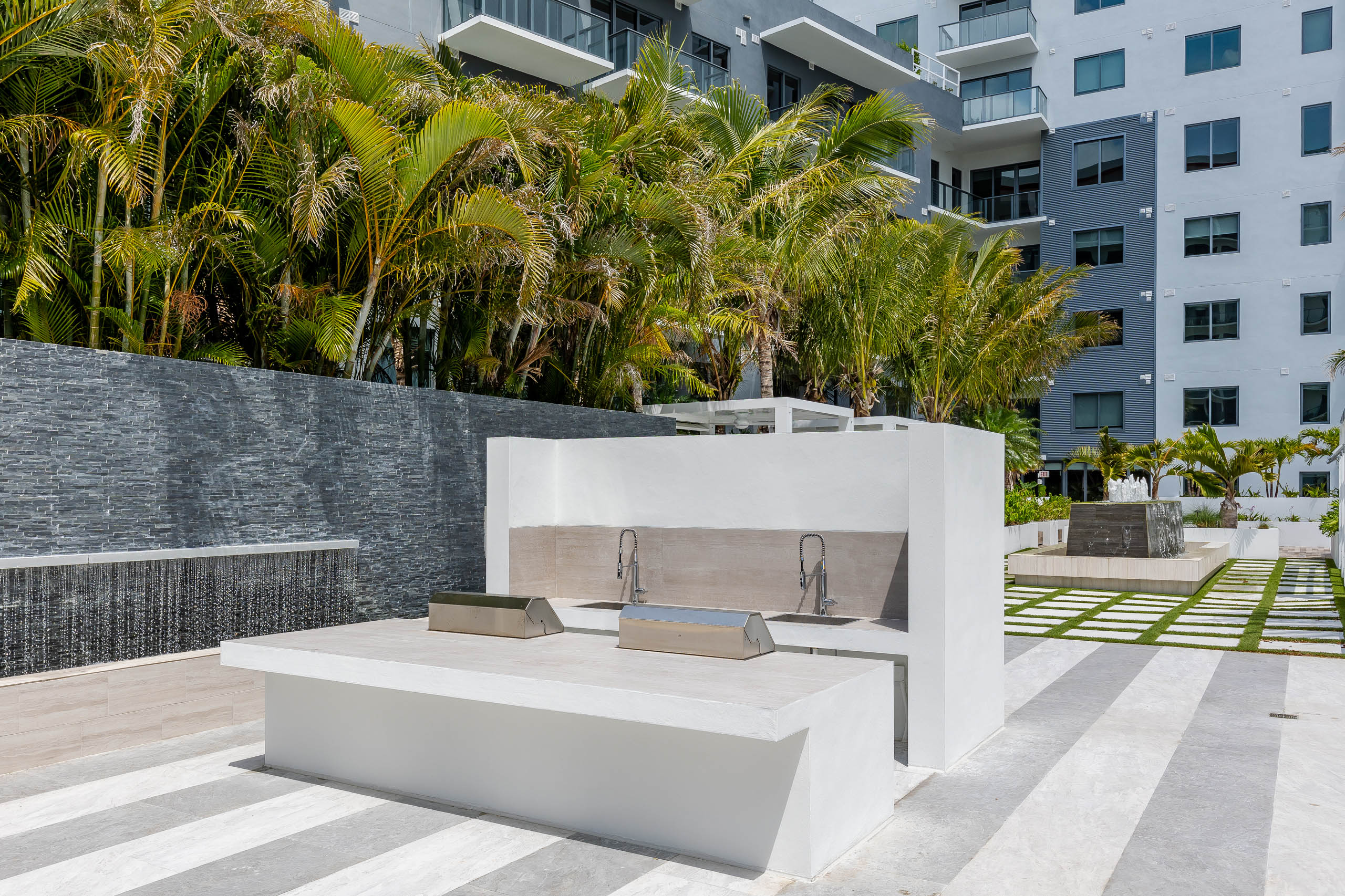 AMLI Midtown Miami apartments grill station with stainless steel grills and cascading water fountains with palm trees 