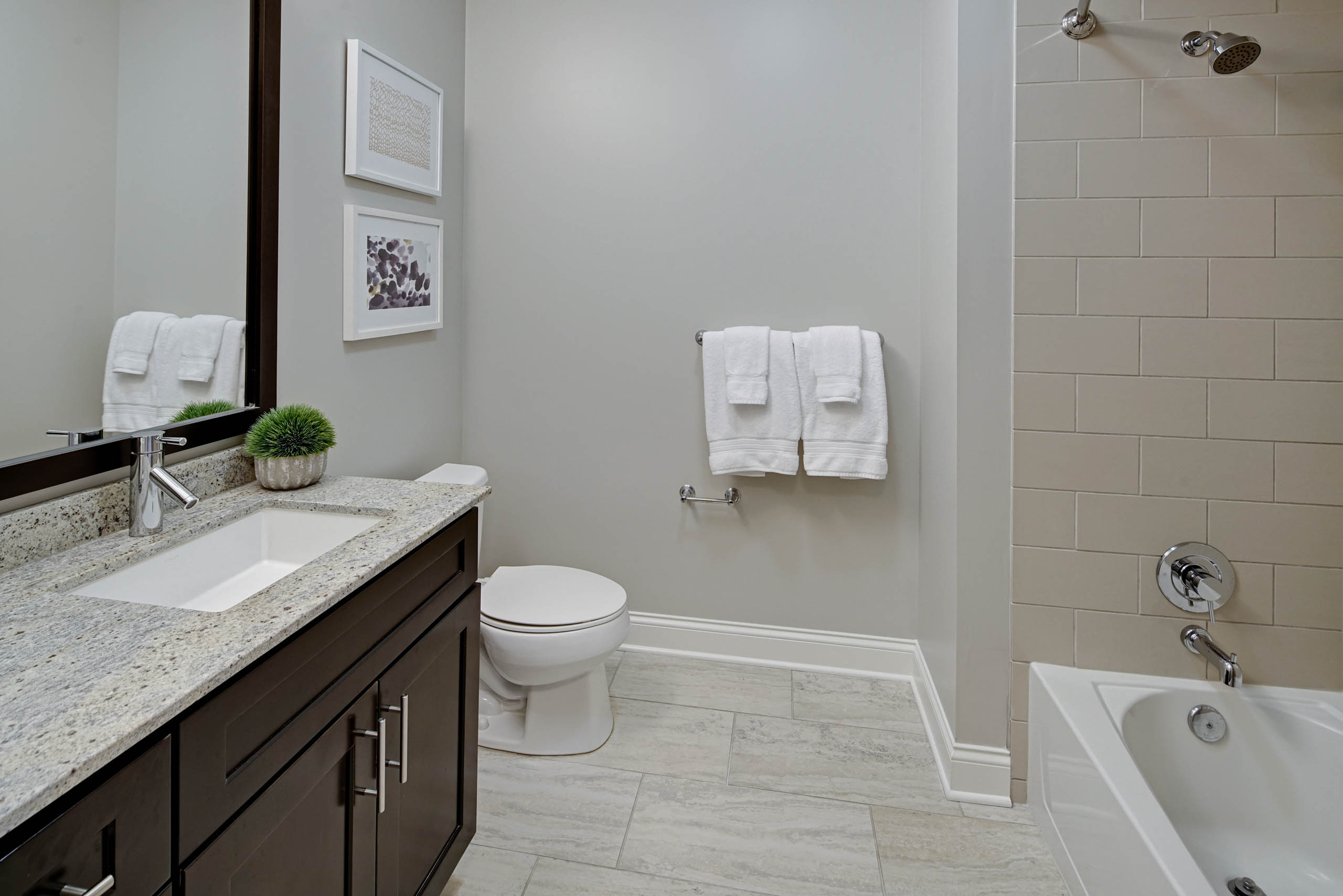 AMLI River North bathroom with dark cabinetry and a granite countertop with light tile flooring and spacious framed mirror