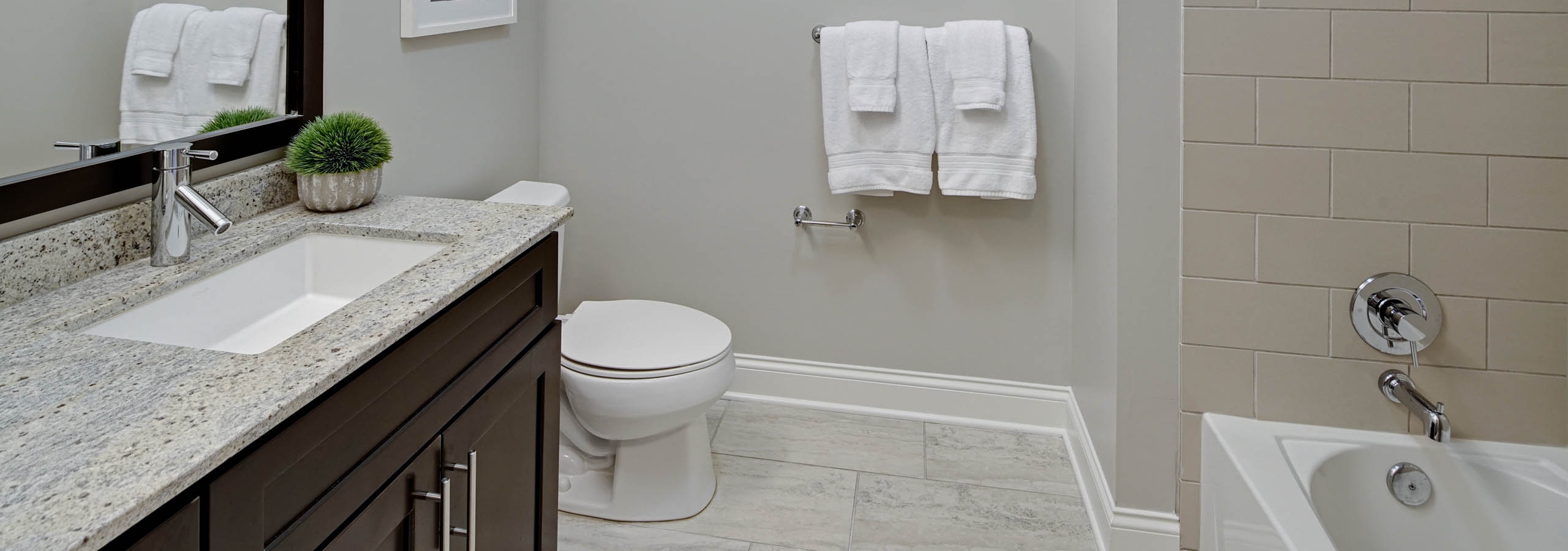 AMLI River North bathroom with dark cabinetry and a granite countertop with light tile flooring and spacious framed mirror