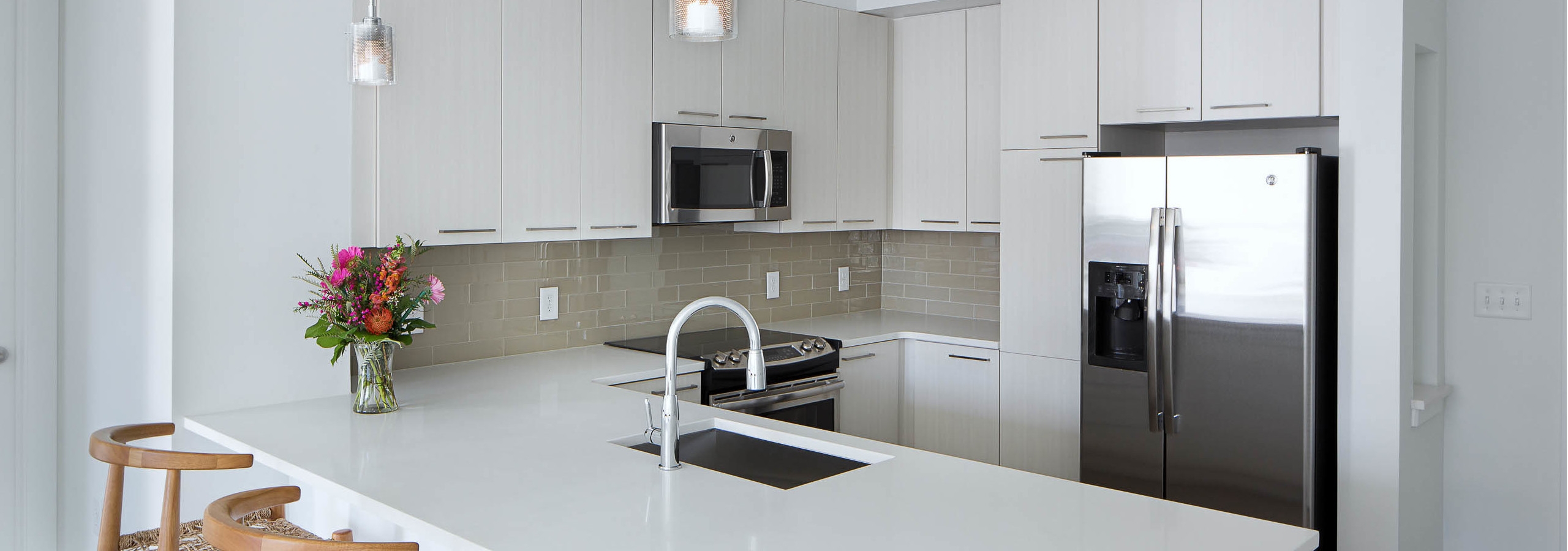 Kitchen at AMLI 3464 with white cabinets and sleek white countertops with a beige backsplash and stainless steel appliances