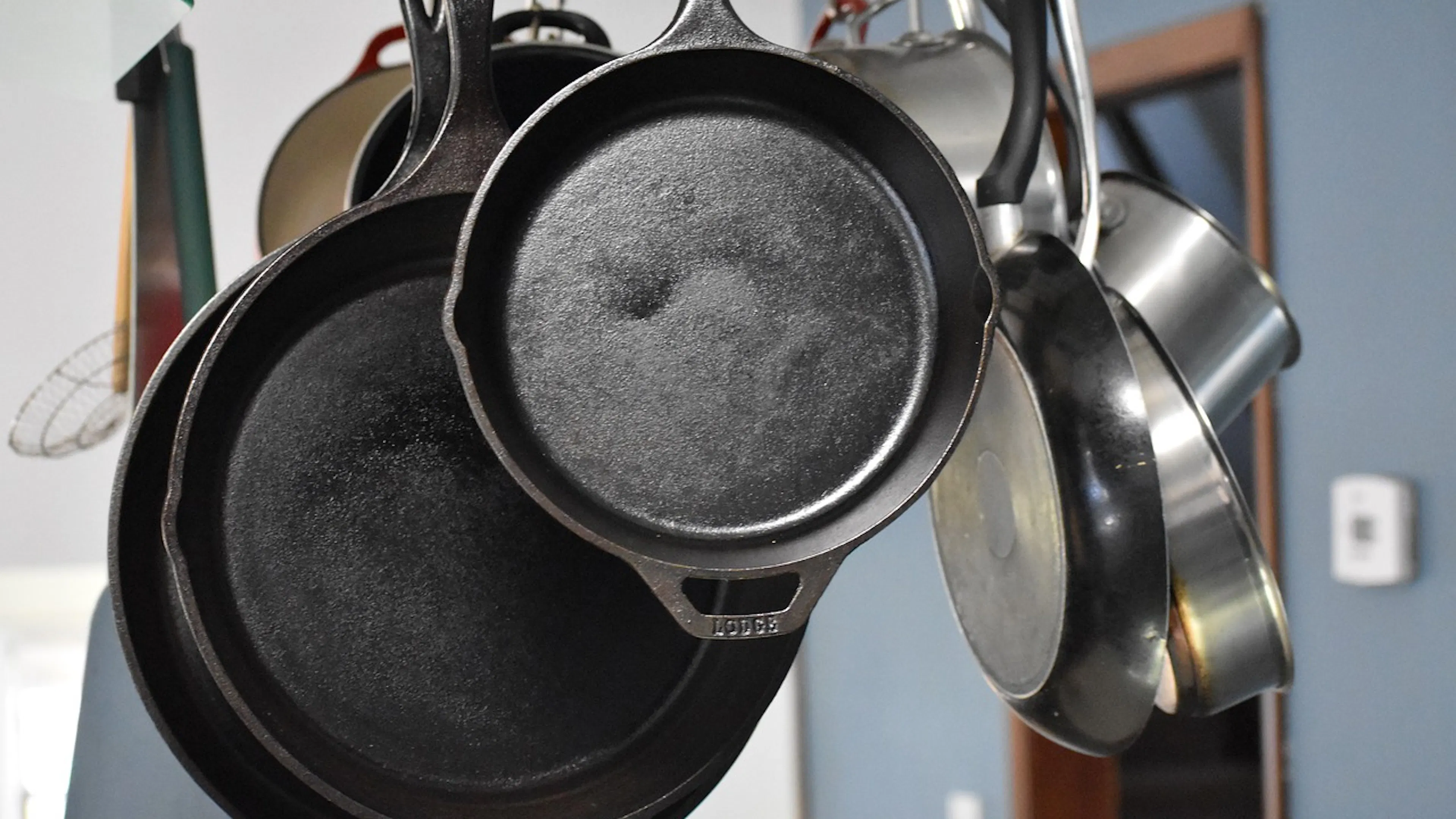 Cast iron pots and pans hanging from ceiling mounted hooks in a blue and white painted kitchen 