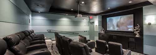 Interior view of media room at AMLI Las Colinas apartment building with three rows of theater seating and large screen