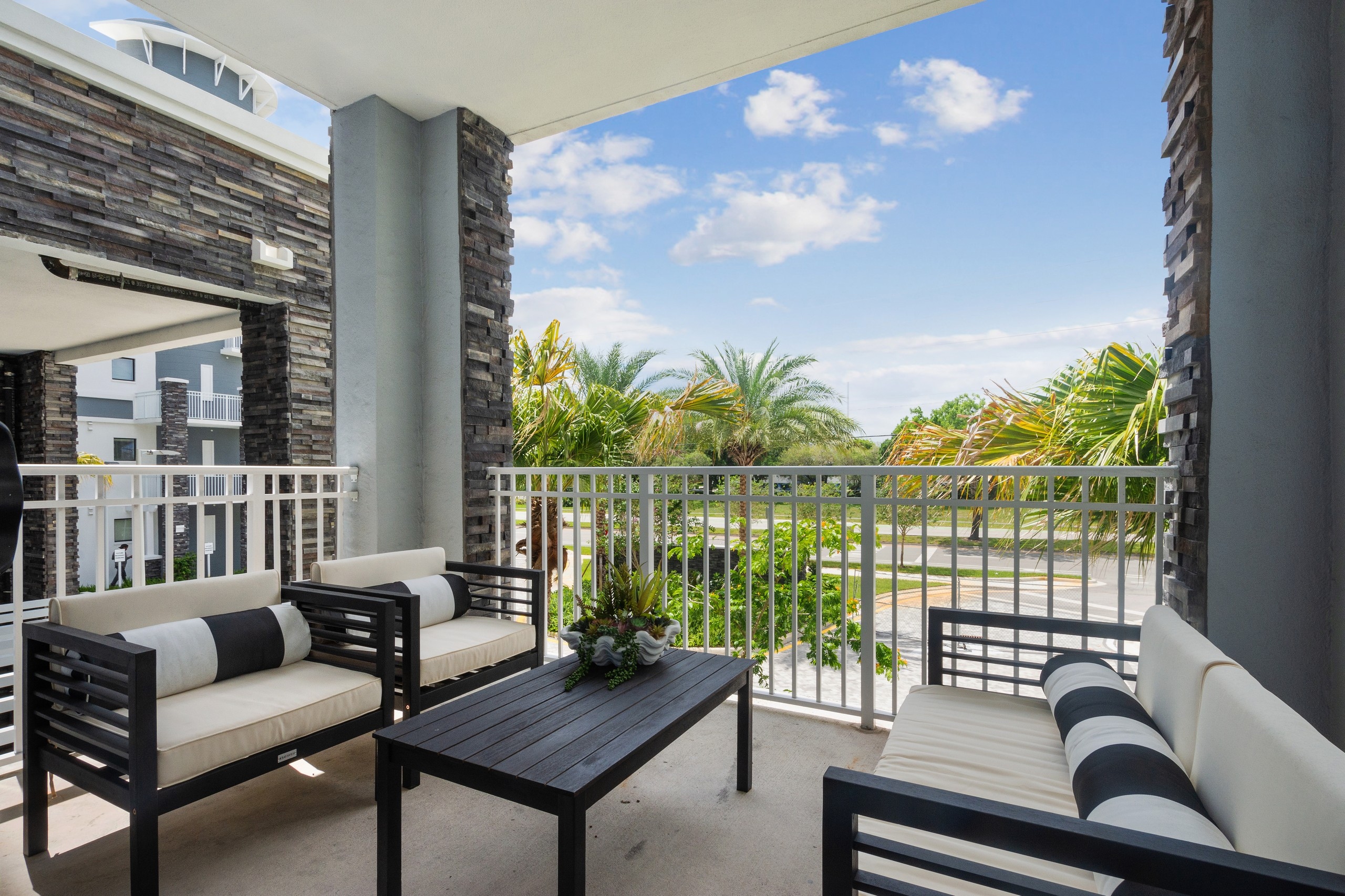 AMLI Park West apartment patio with brown metal table and 2 chairs and sofa with white cushions and striped accent pillows 