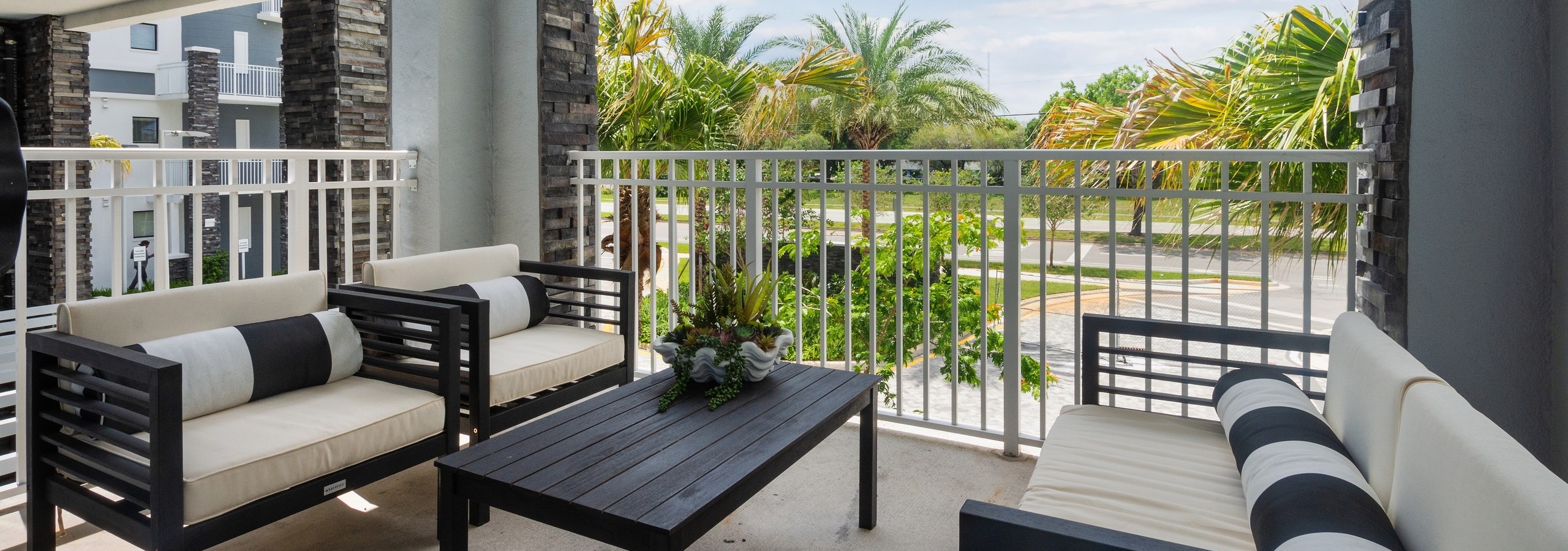 AMLI Park West apartment patio with brown metal table and 2 chairs and sofa with white cushions and striped accent pillows
