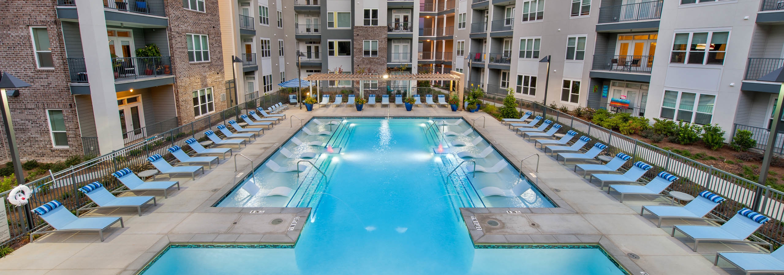 Exterior of AMLI Piedmont Heights pool at dusk featuring in water ledge loungers framed by lounge chairs and bright plants