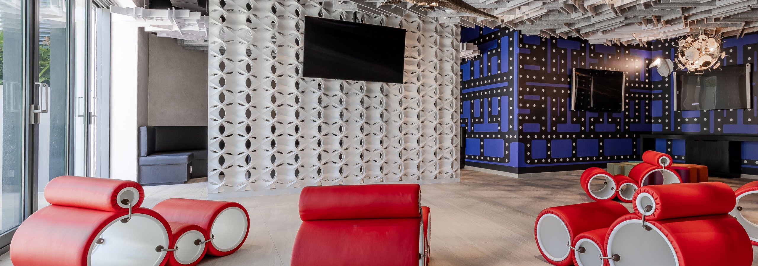 Ultra modern game lounge at AMLI Midtown Miami apartments with red circular chairs and TVs and geometric walls and ceiling