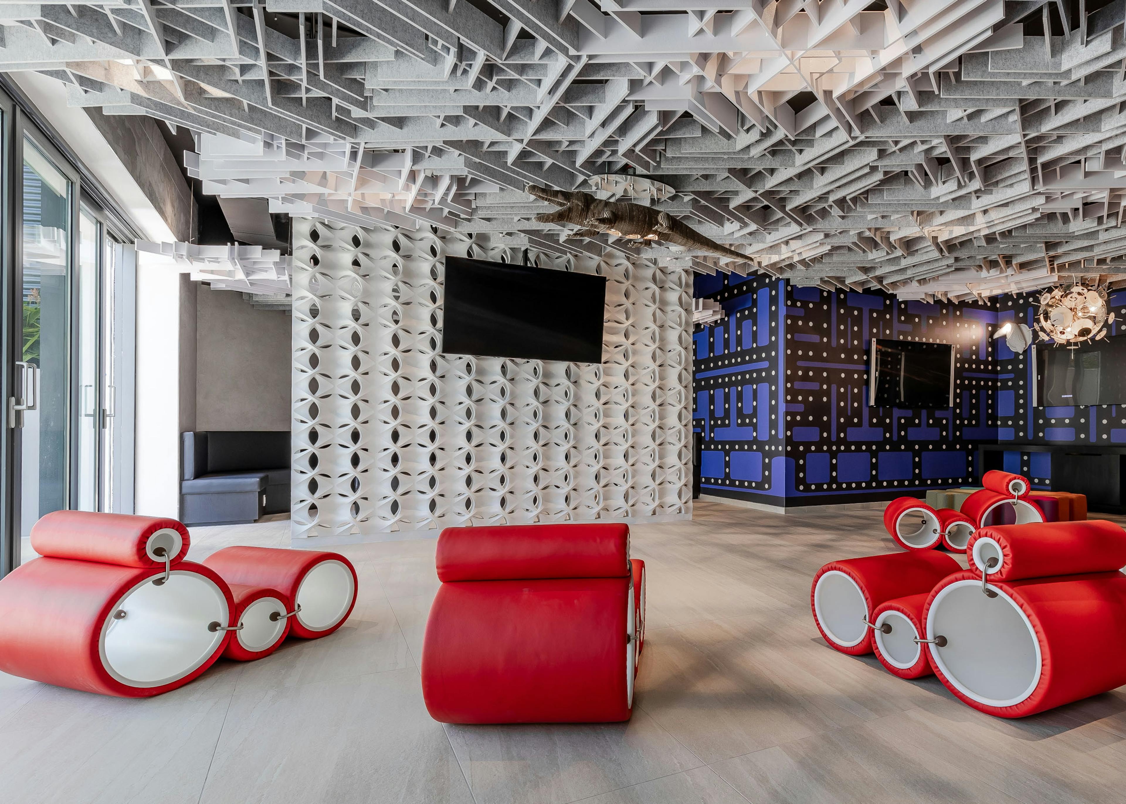 Ultra modern game lounge at AMLI Midtown Miami apartments with red circular chairs and TVs and geometric walls and ceiling