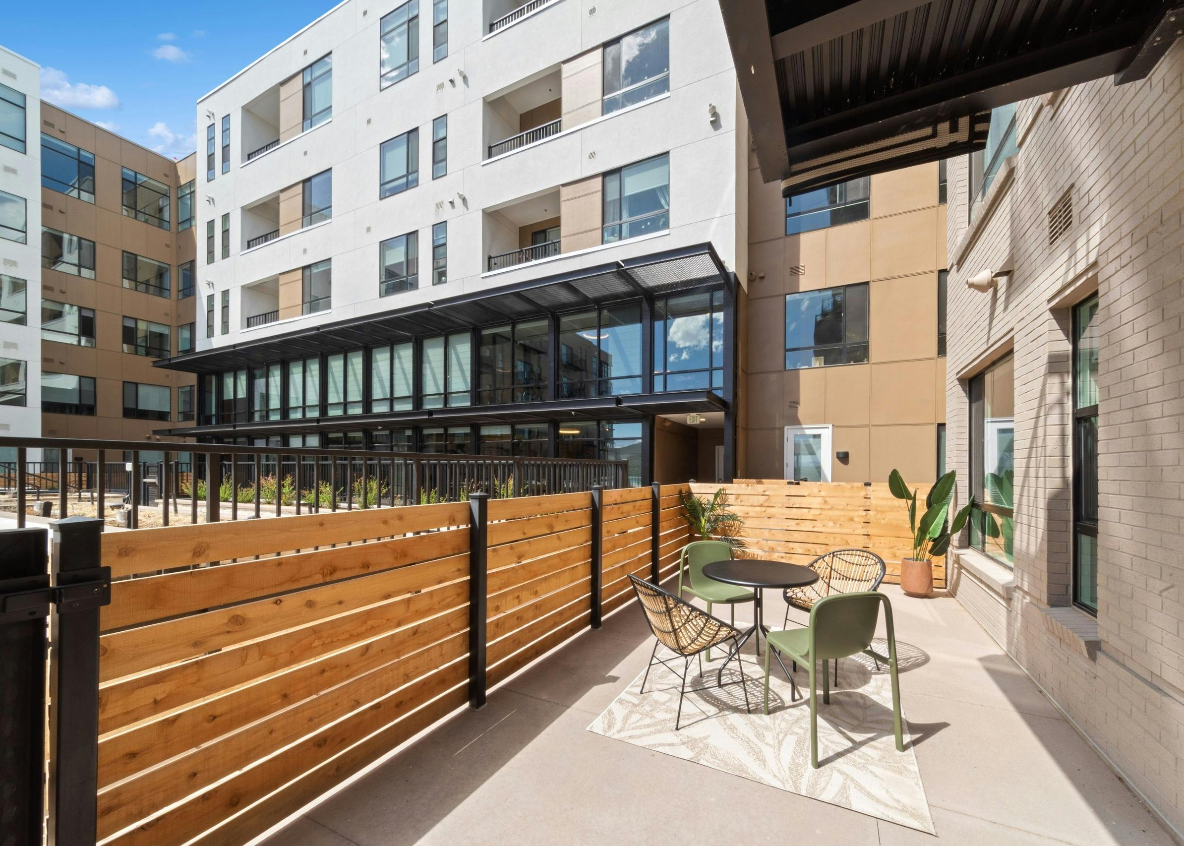 Exterior view of an apartment patio at AMLI Broadway Park featuring a natural wood fence and a small dining table with chairs