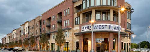 Exterior view of AMLI West Plano at nighttime with brick facade and lamp posts and trees neatly lining the building