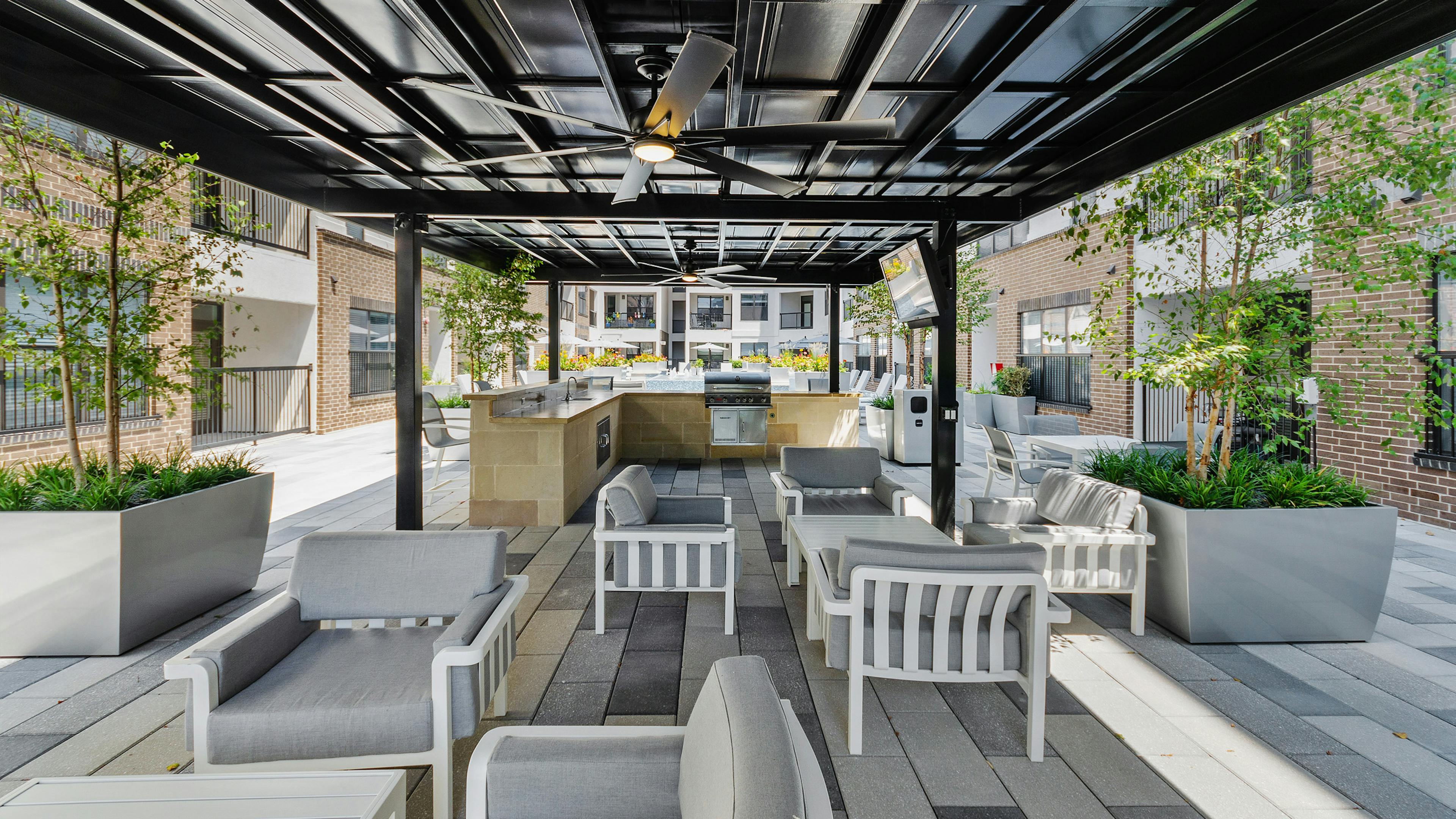 Grill station and outdoor kitchen at AMLI Quadrangle apartments with gray seating and white tables and black cabana overhead