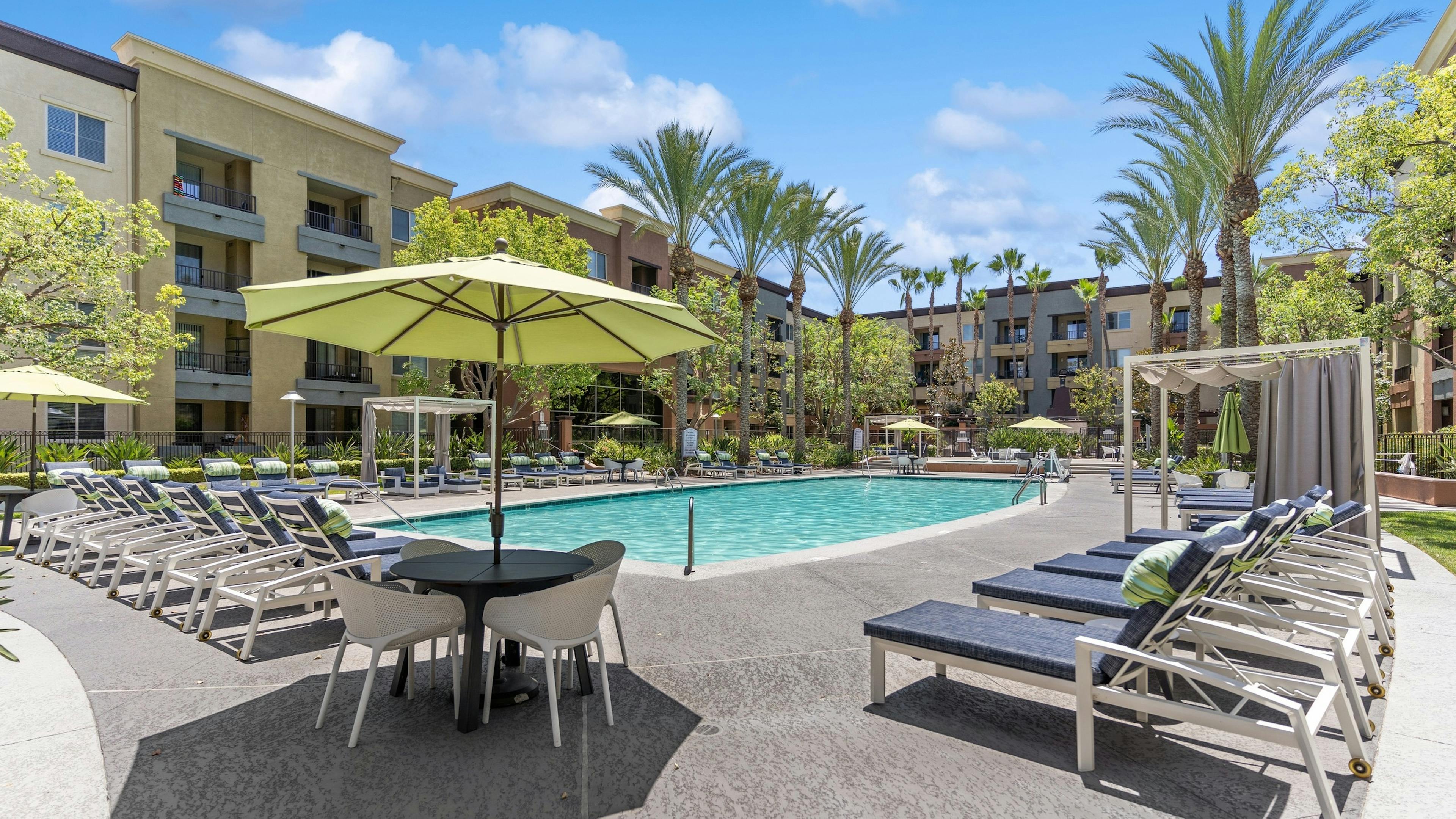 AMLI Warner Center resort style swimming pool with blue lounge chairs and private cabanas with umbrella shaded dining tables