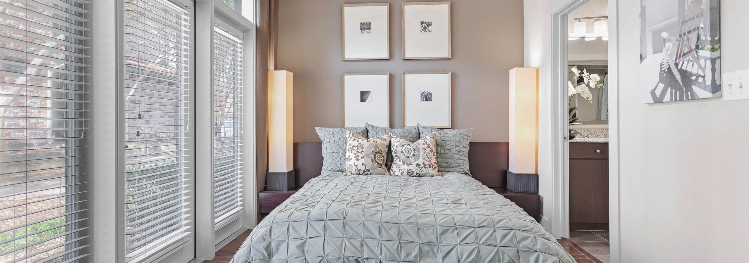 Apartment bedroom at AMLI at Escena with three large windows and a bed covered in colorful pillows and flanked by tall lights