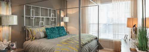 Interior view of AMLI Memorial Heights apartment bedroom with silver canopy bed and large window with blinds and curtains