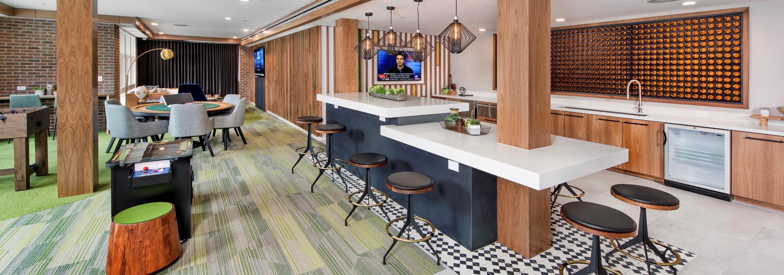 Clubroom at AMLI Decatur with serving kitchen and an arcade game with a poker table and big screen TV on green carpet