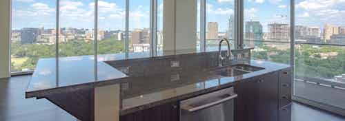 Interior view of empty AMLI Design District apartment living room from kitchen with floor to ceiling windows and city view