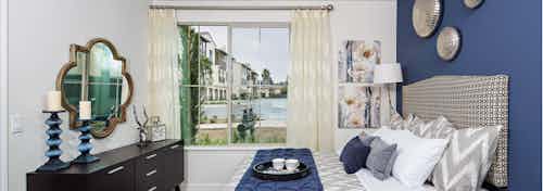 Interior view of AMLI Spanish Hills bedroom with patterned queen upholstered headboard, dresser and window with curtains