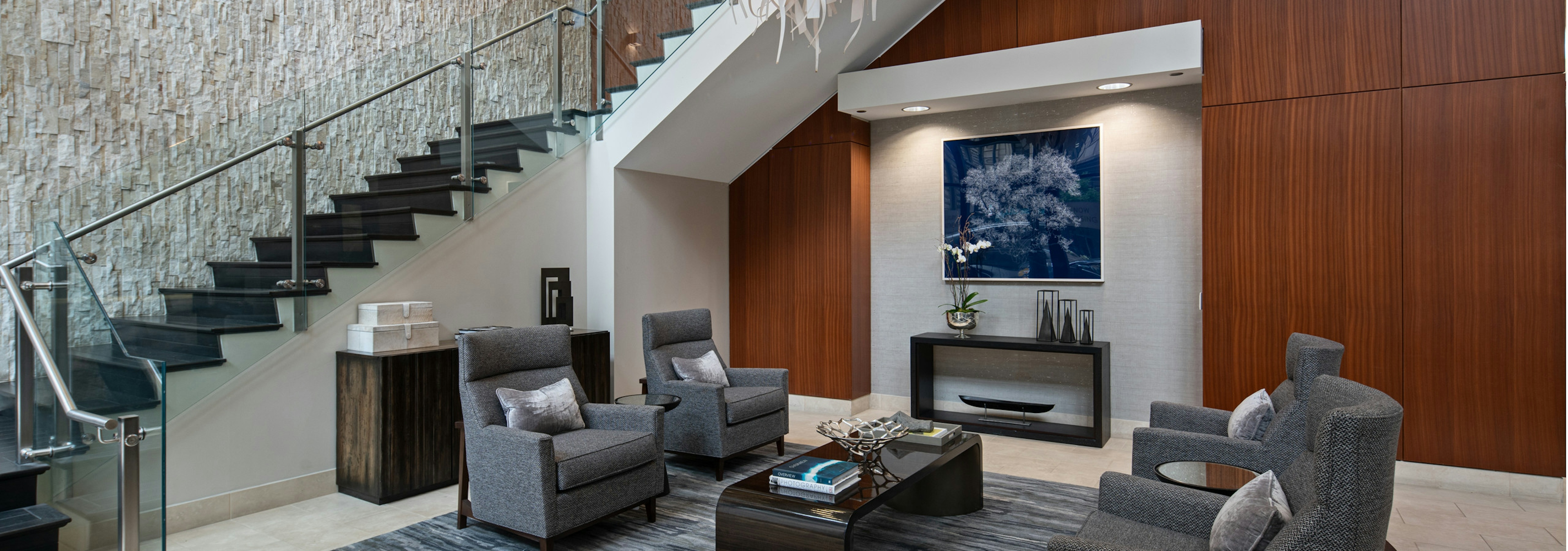 AMLI River North lobby with a cherry wood accent wall and grey seating in front of a modern wrap around staircase 