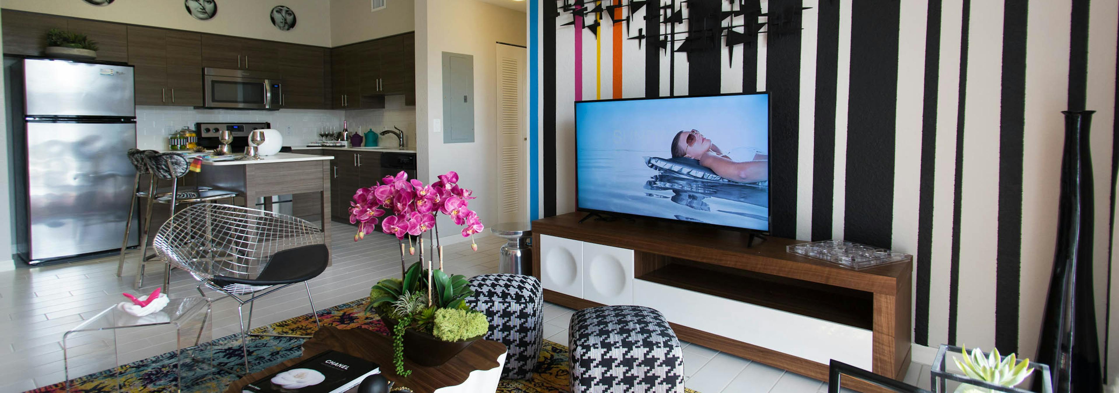 AMLI Dadeland apartment living area with black and white wall, TV on console, hounds tooth stools and a peek into the kitchen