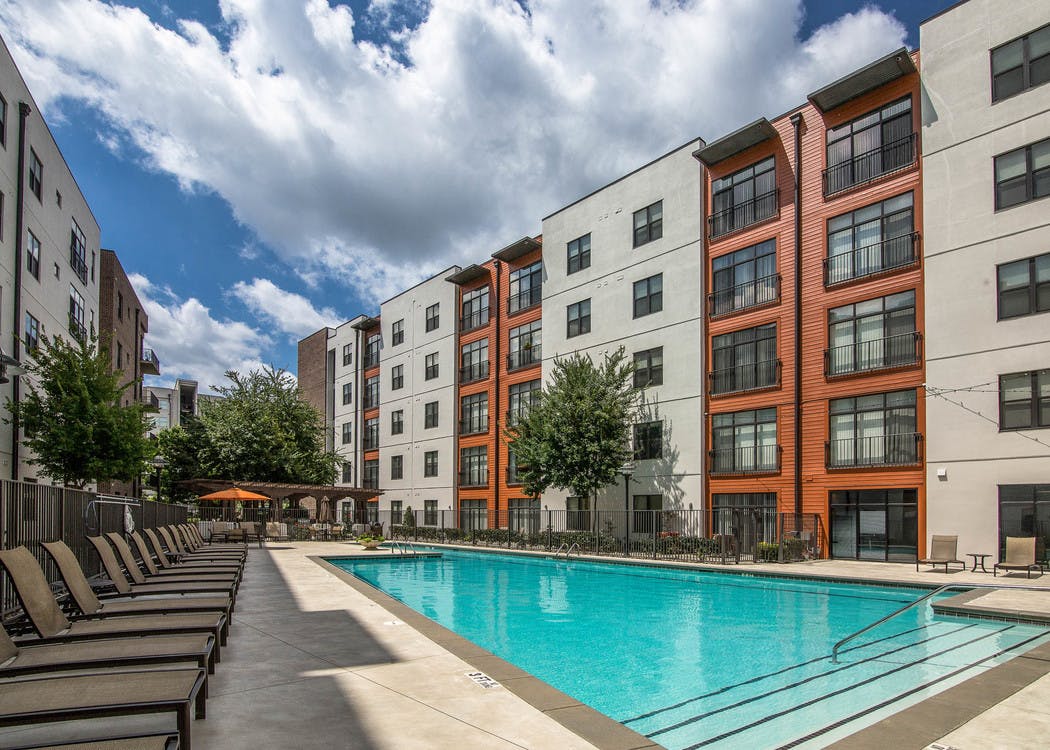 Sunny daytime view of a swimming pool surrounded by tan lounge chairs on both sides of the water at AMLI 4th Ward