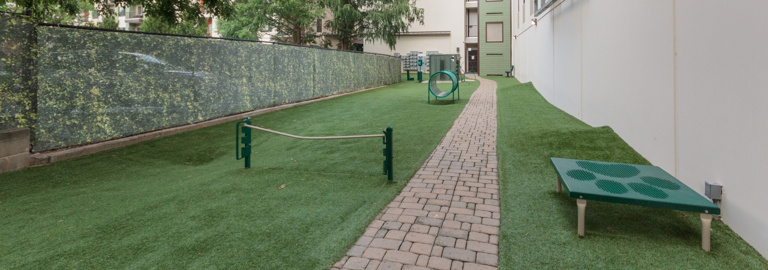 Outdoor grassy paw park next to AMLI Ponce Park apartment building with tunnel and other obstacles for dogs to play with