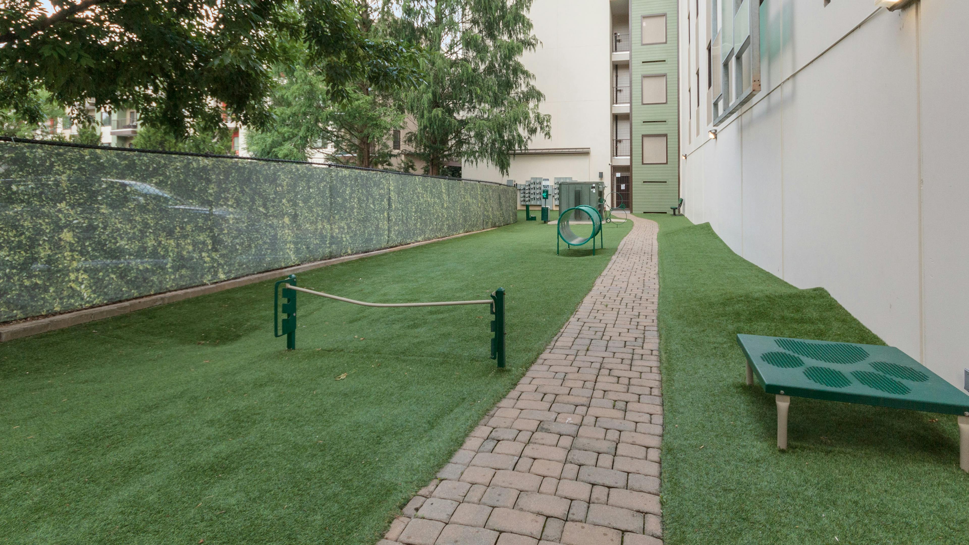 Outdoor grassy paw park next to AMLI Ponce Park apartment building with tunnel and other obstacles for dogs to play with