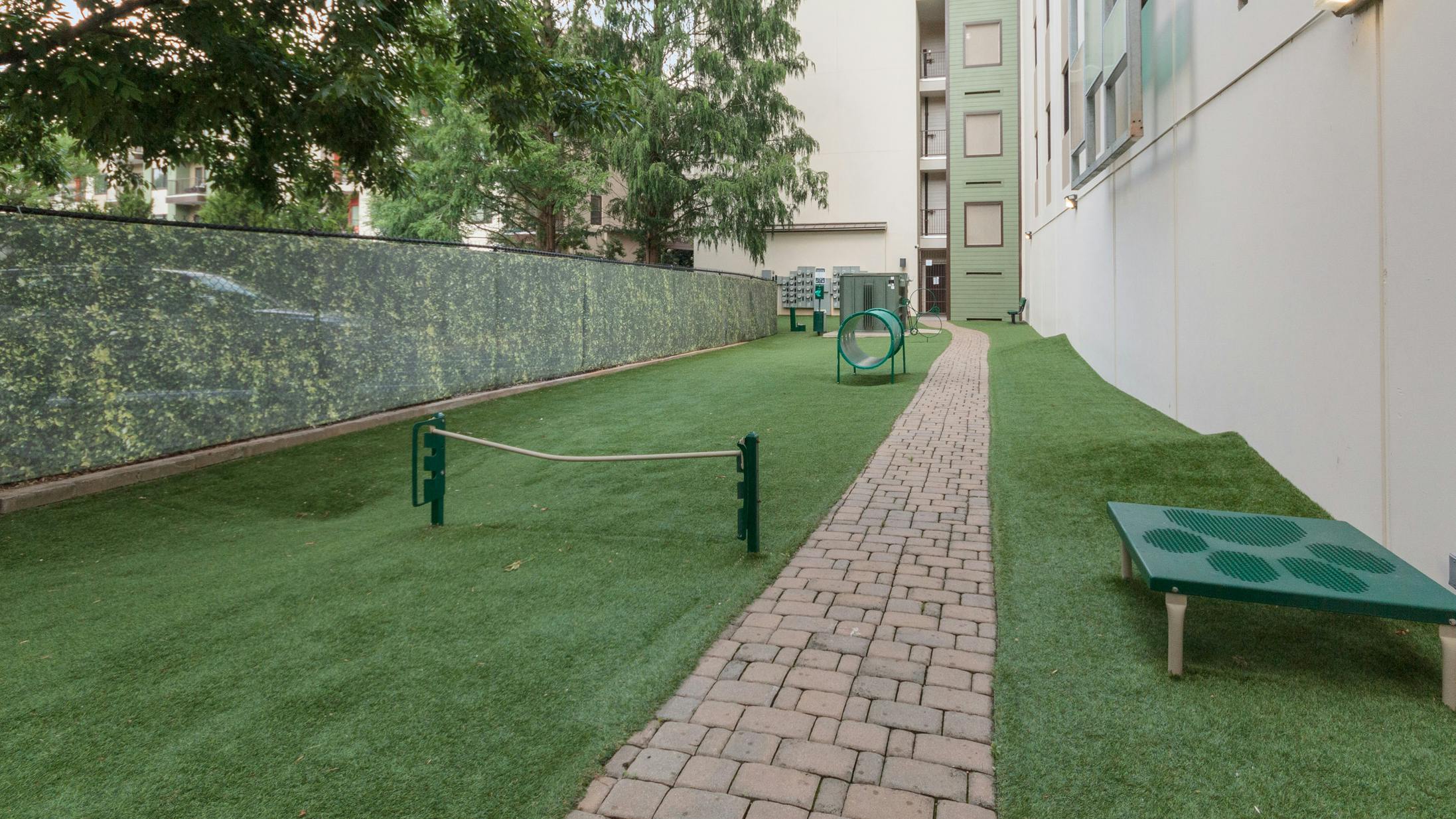 Outdoor grassy paw park next to AMLI Ponce Park apartment building with tunnel and other obstacles for dogs to play with