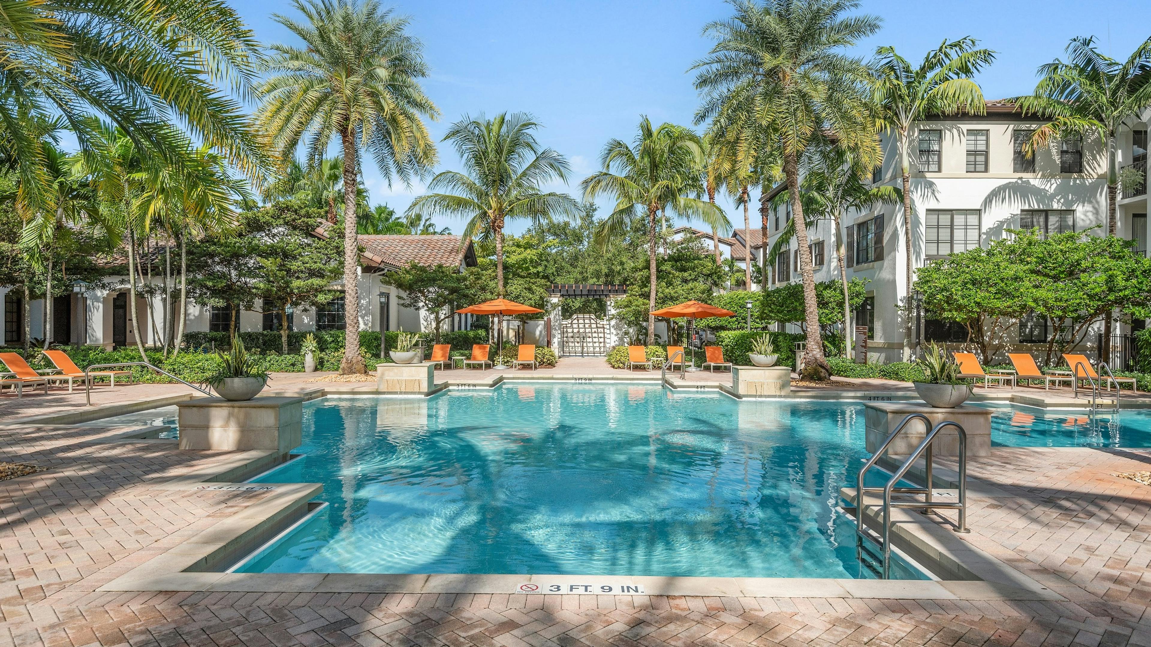AMLI Toscana Place swimming pool surrounded by lush palm trees and orange lounge chairs and white buildings