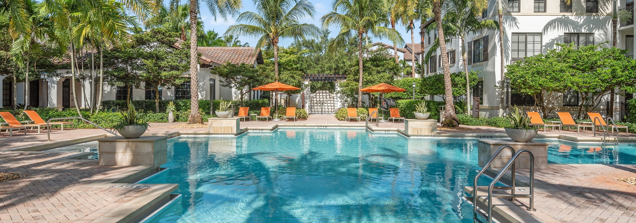 AMLI Toscana Place swimming pool surrounded by lush palm trees and orange lounge chairs and white buildings