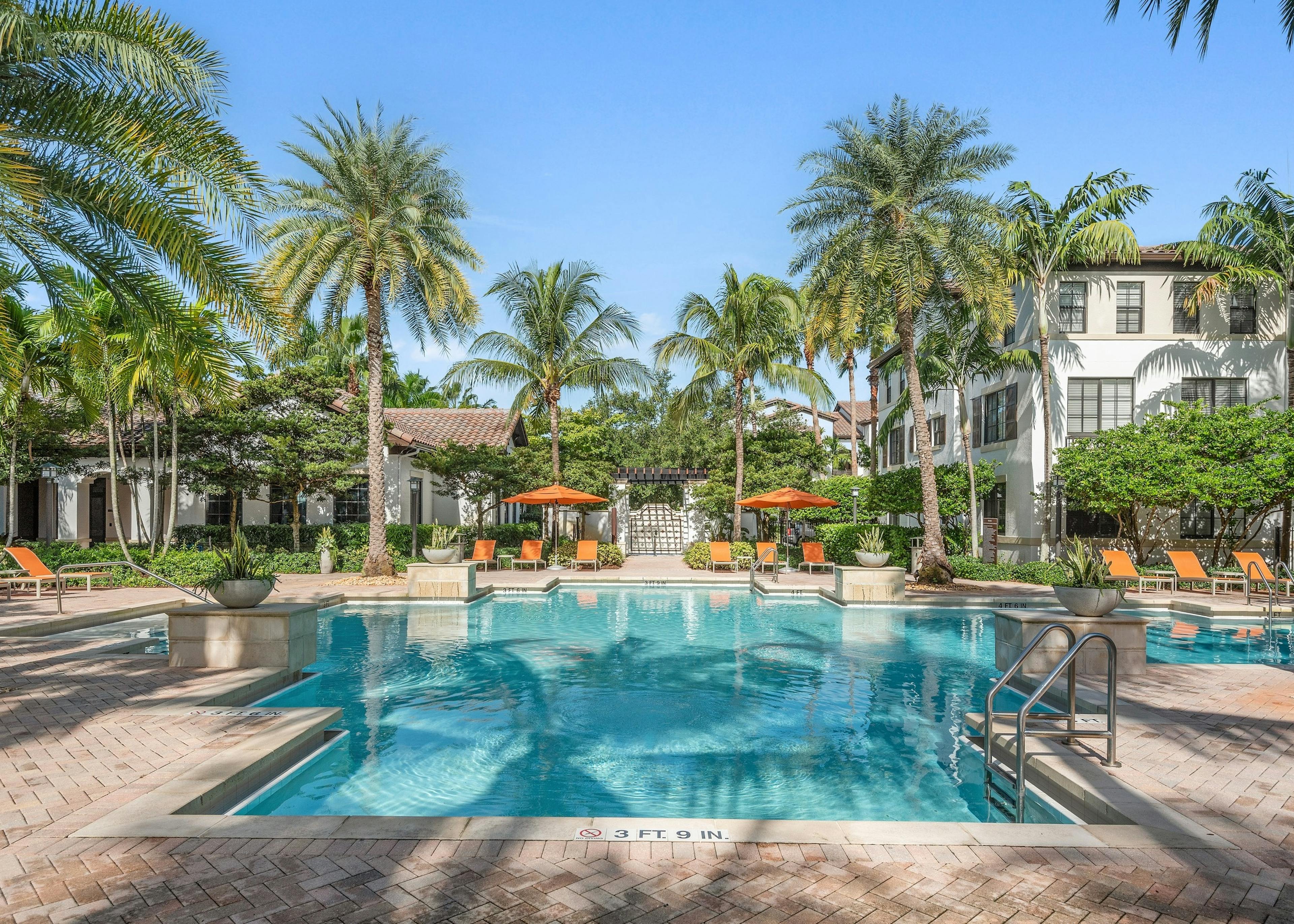 AMLI Toscana Place swimming pool surrounded by lush palm trees and orange lounge chairs and white buildings
