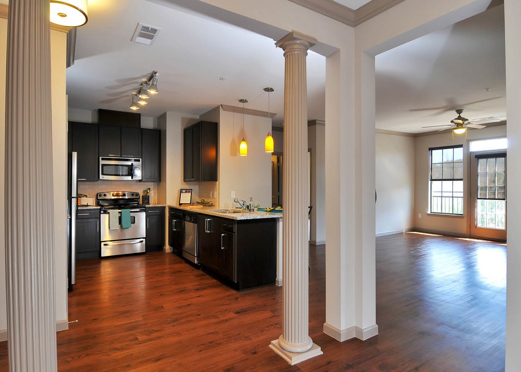 AMLI North Point kitchen with dark cabinets and modern light fixtures with empty living area and windows in the background