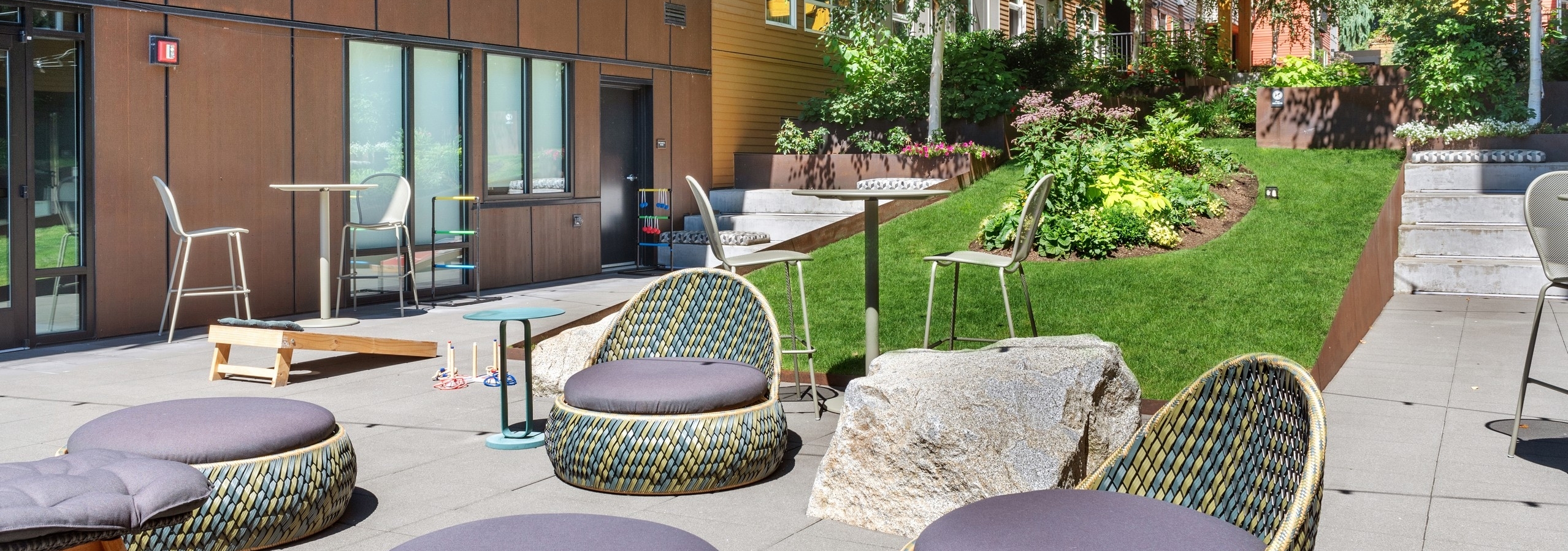 Exterior view of a courtyard at AMLI Wallingford with chairs and ottomans and cornhole boards and market lights overhead