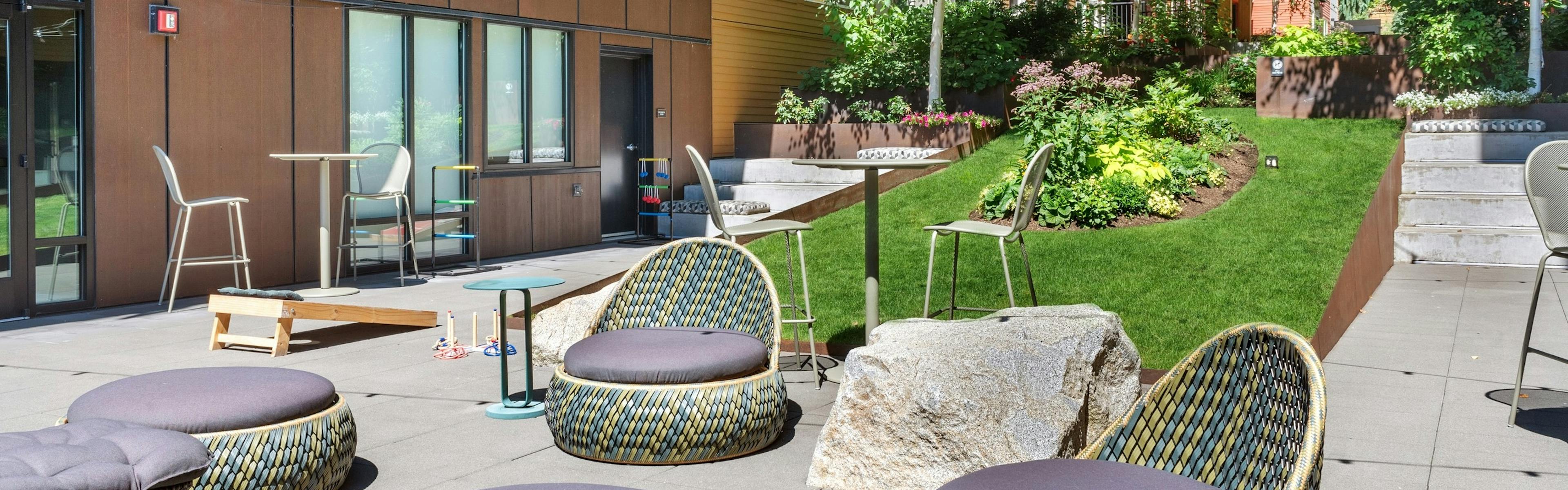 Exterior view of a courtyard at AMLI Wallingford with chairs and ottomans and cornhole boards and market lights overhead