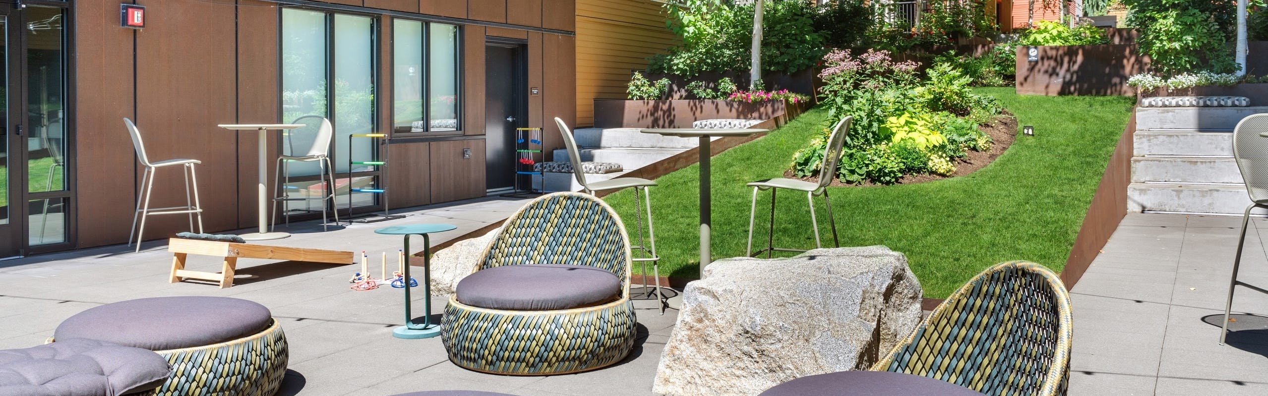Exterior view of a courtyard at AMLI Wallingford with chairs and ottomans and cornhole boards and market lights overhead