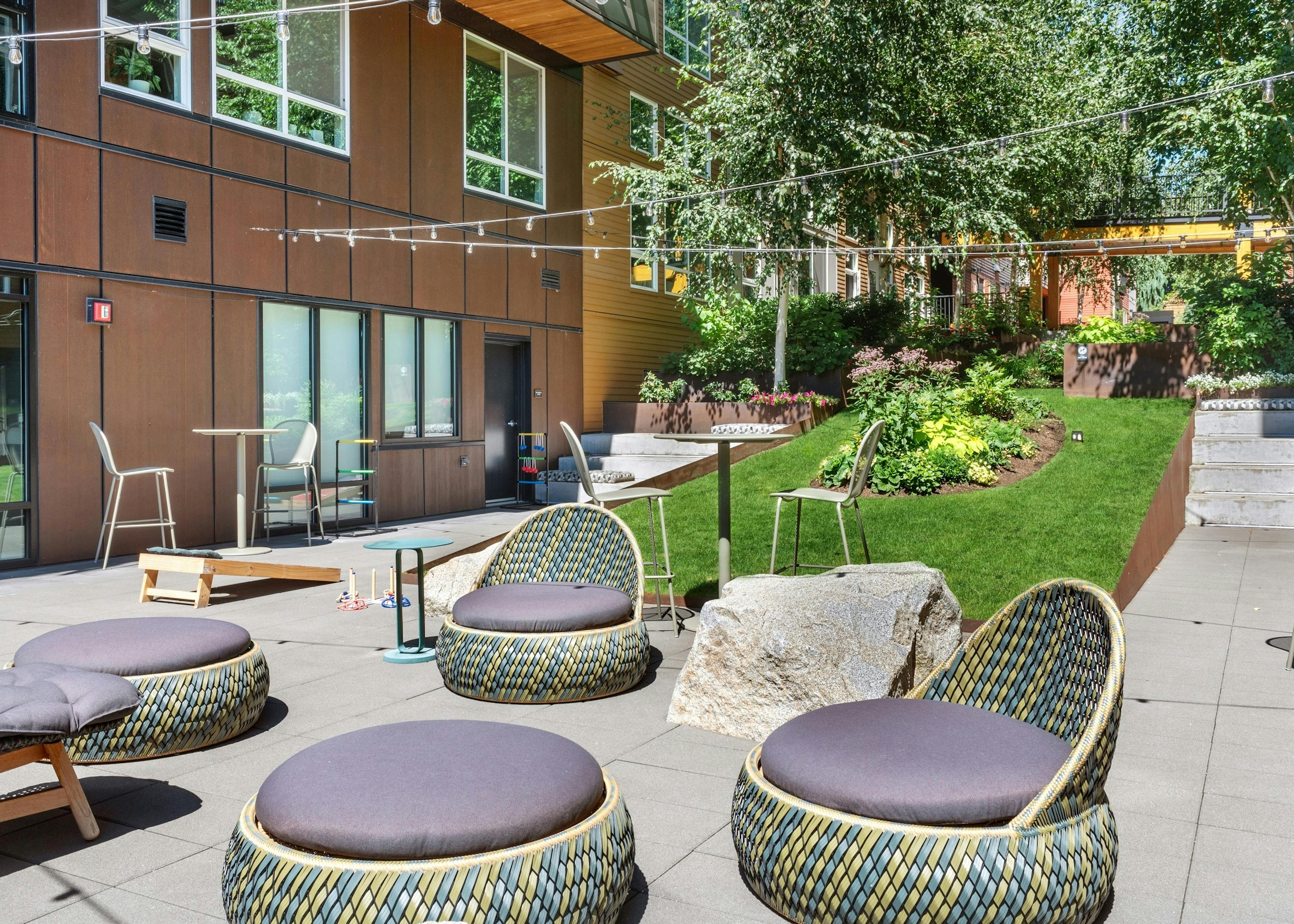 Exterior view of a courtyard at AMLI Wallingford with chairs and ottomans and cornhole boards and market lights overhead