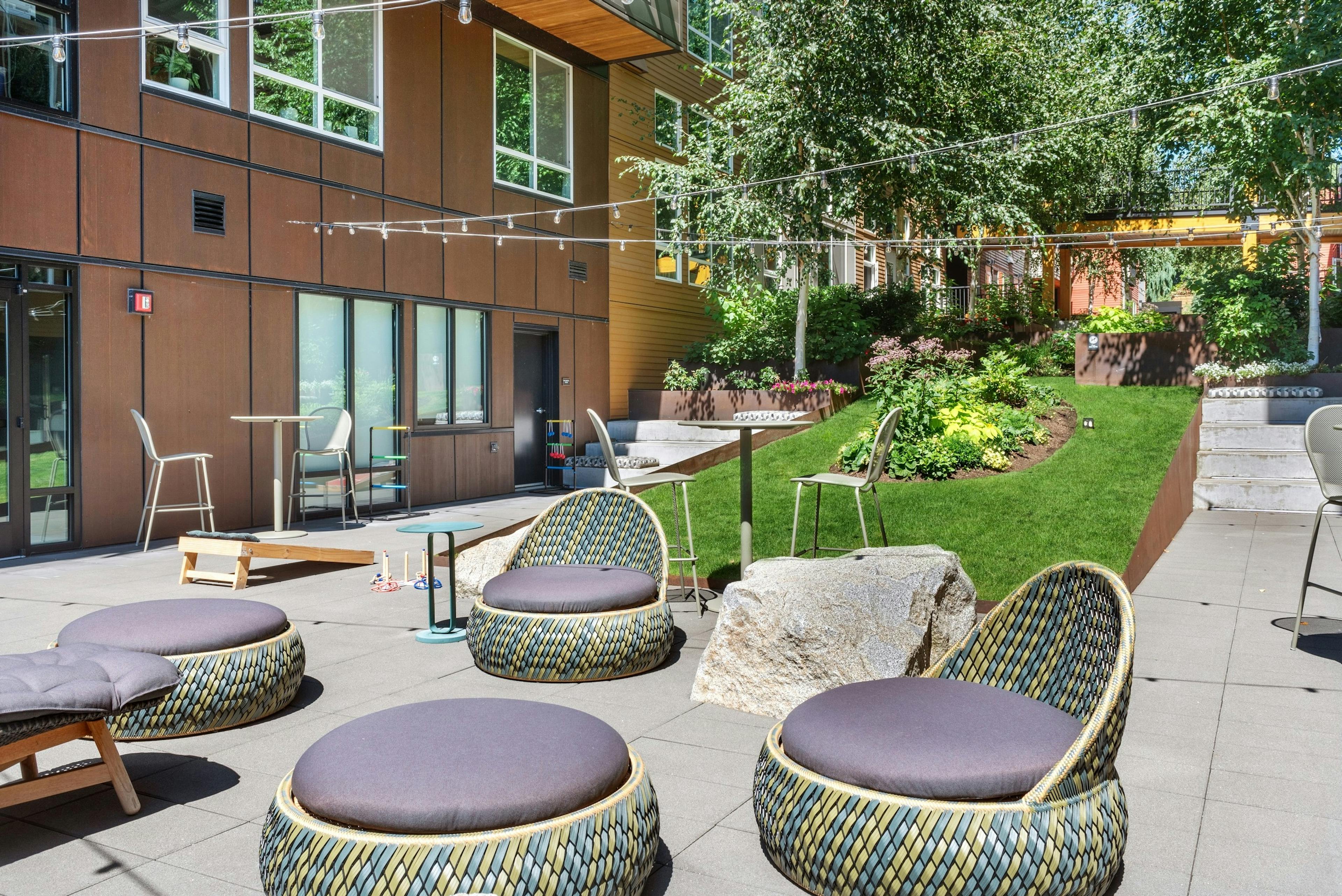 Exterior view of a courtyard at AMLI Wallingford with chairs and ottomans and cornhole boards and market lights overhead