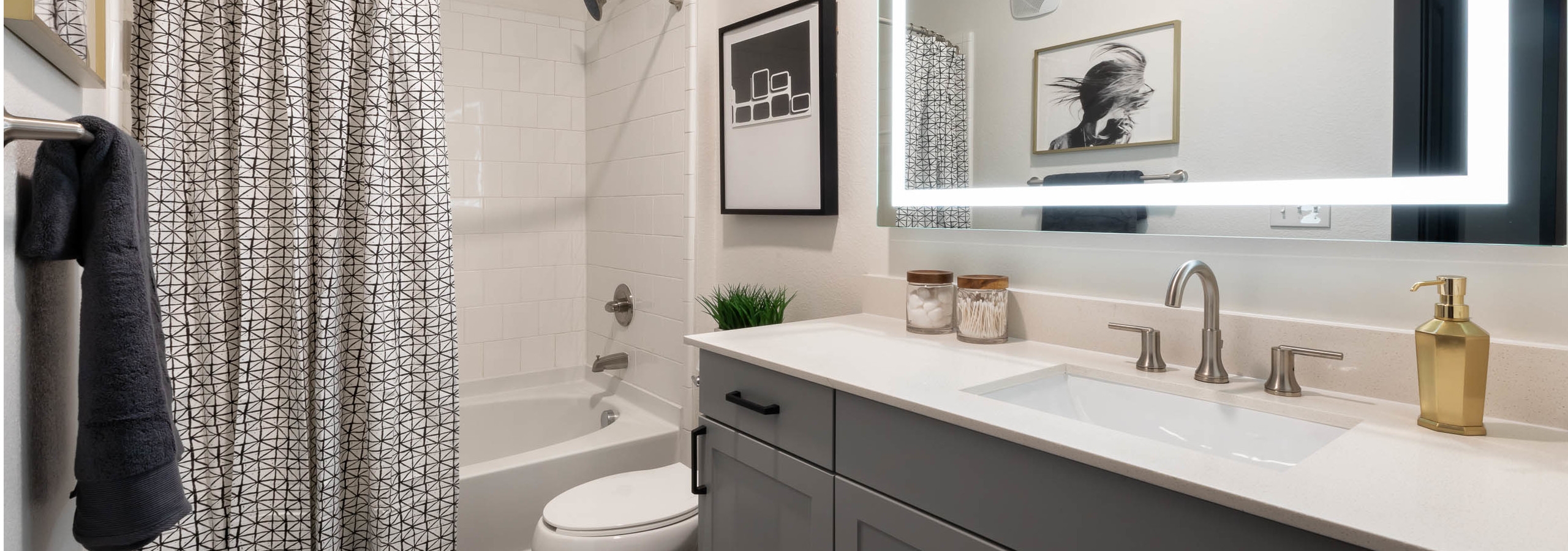 AMLI Quadrangle bathroom with grey vanity and a white countertop with a toilet and shower tub with black and white curtain