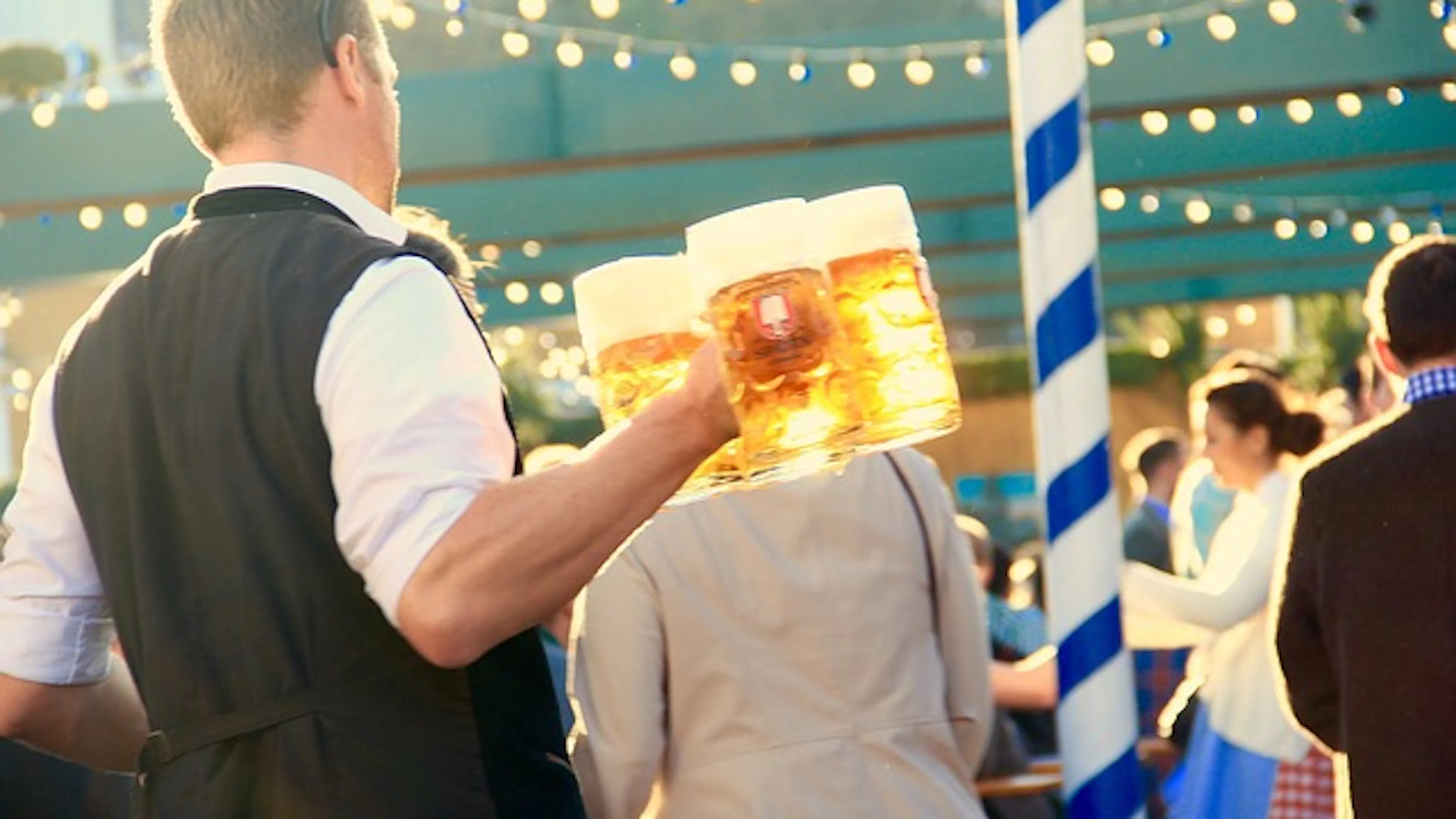 A waiter holding three steins of beer and walking through an outdoor festival